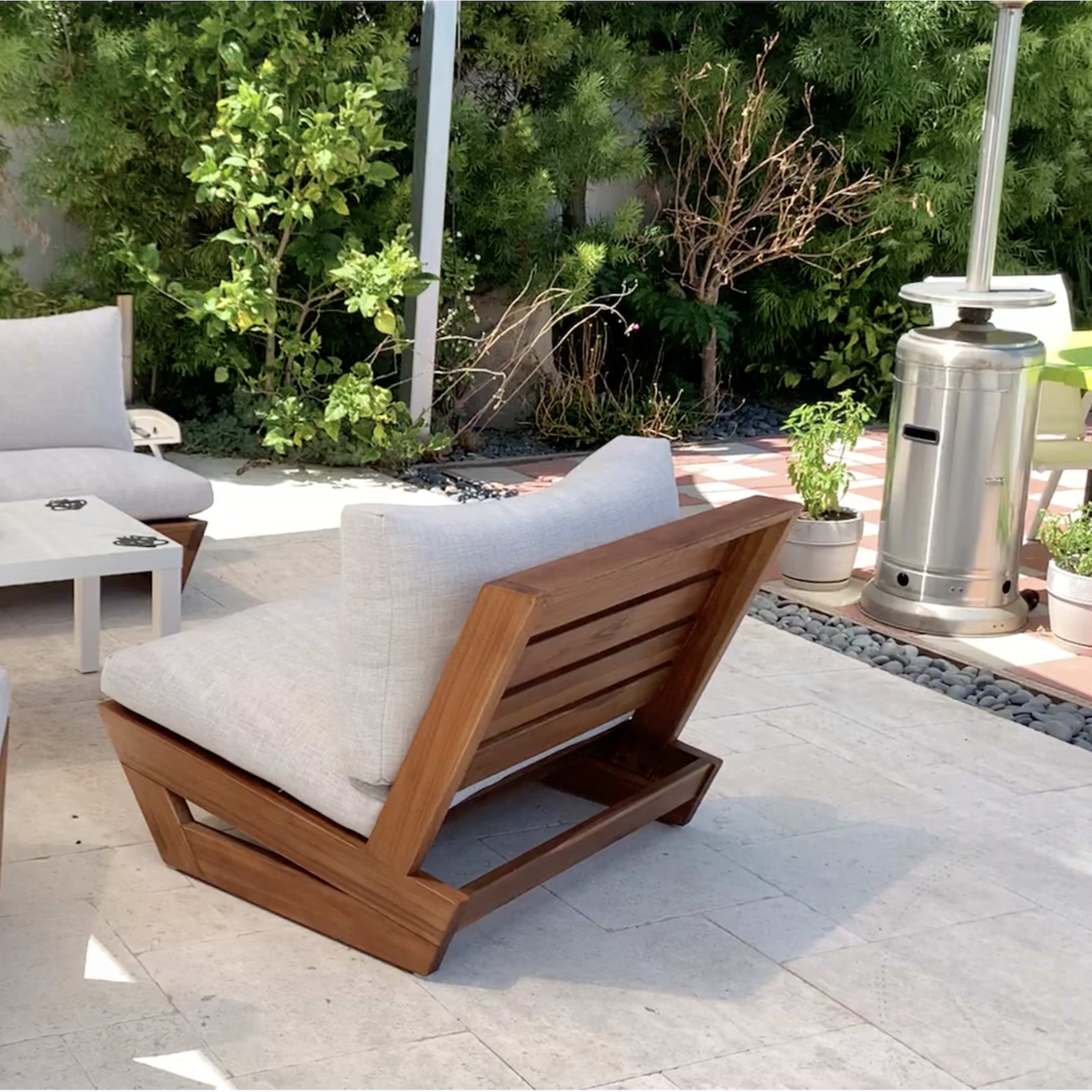 A patio seating arrangement consisting of a sectional sofa and two armchairs, surrounded by greenery and a stone floor.