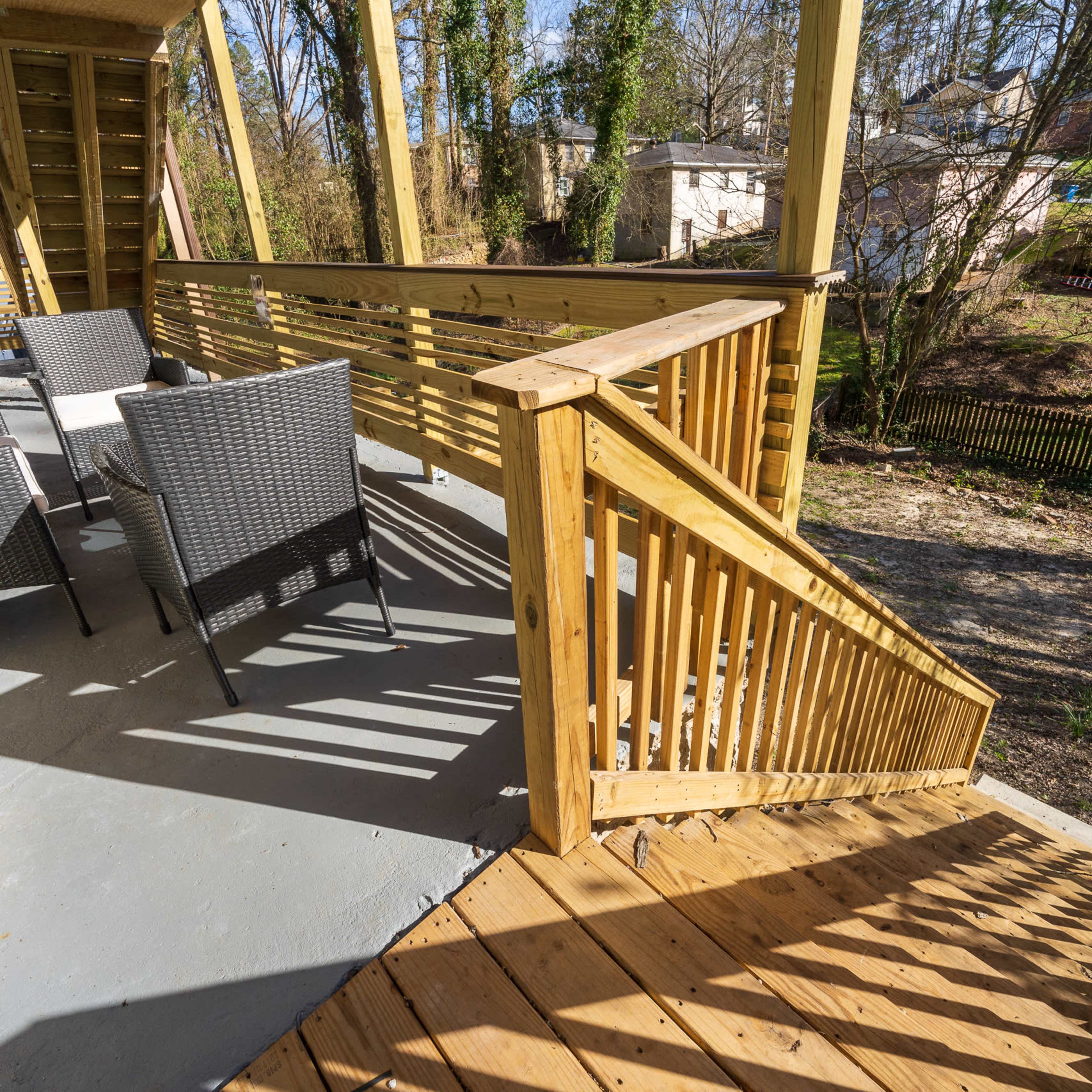 A wooden deck with a staircase leading down, surrounded by trees and a view of a grassy area below.