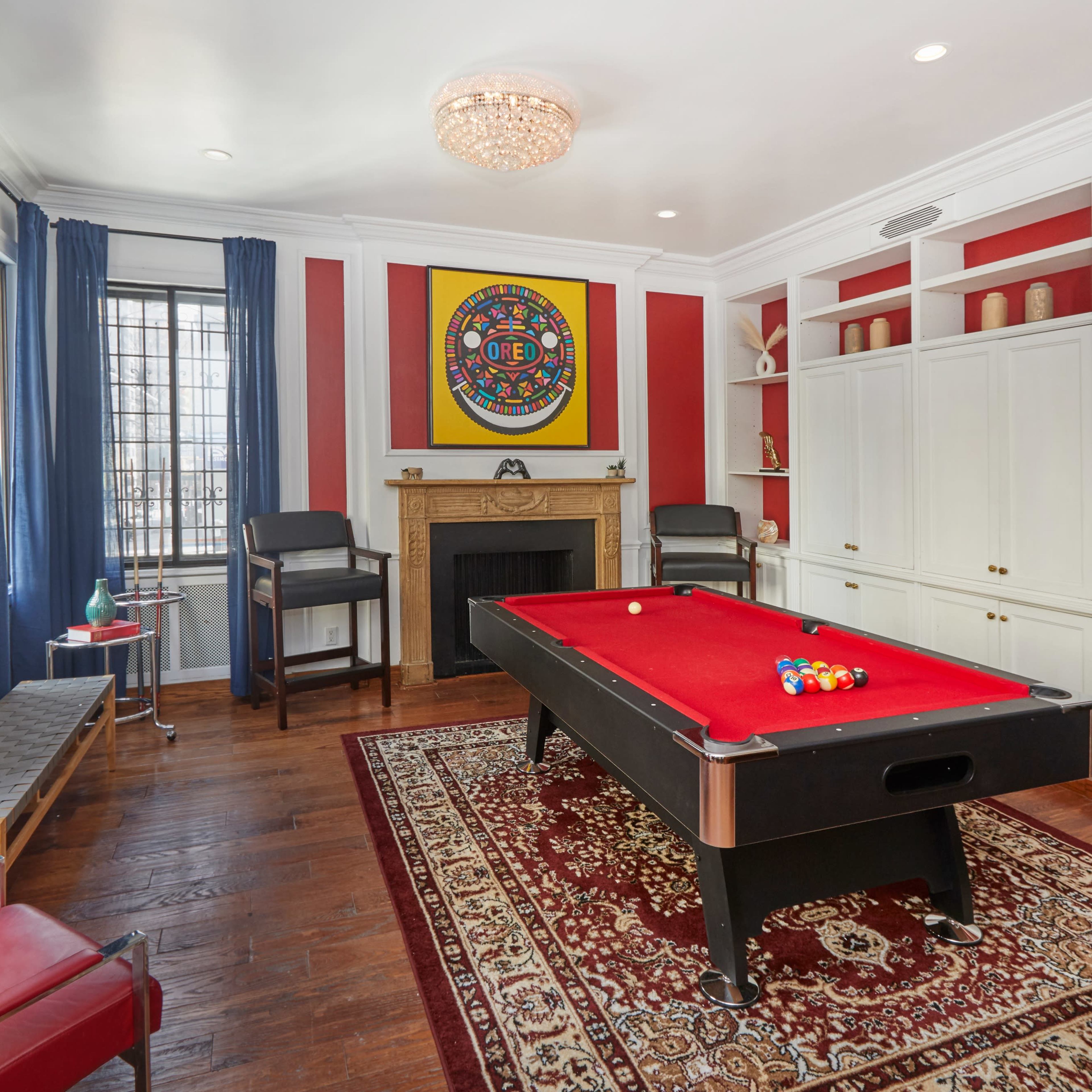 A game room featuring a red felt pool table, a decorative rug, a fireplace, and built-in shelving with various decorative items.