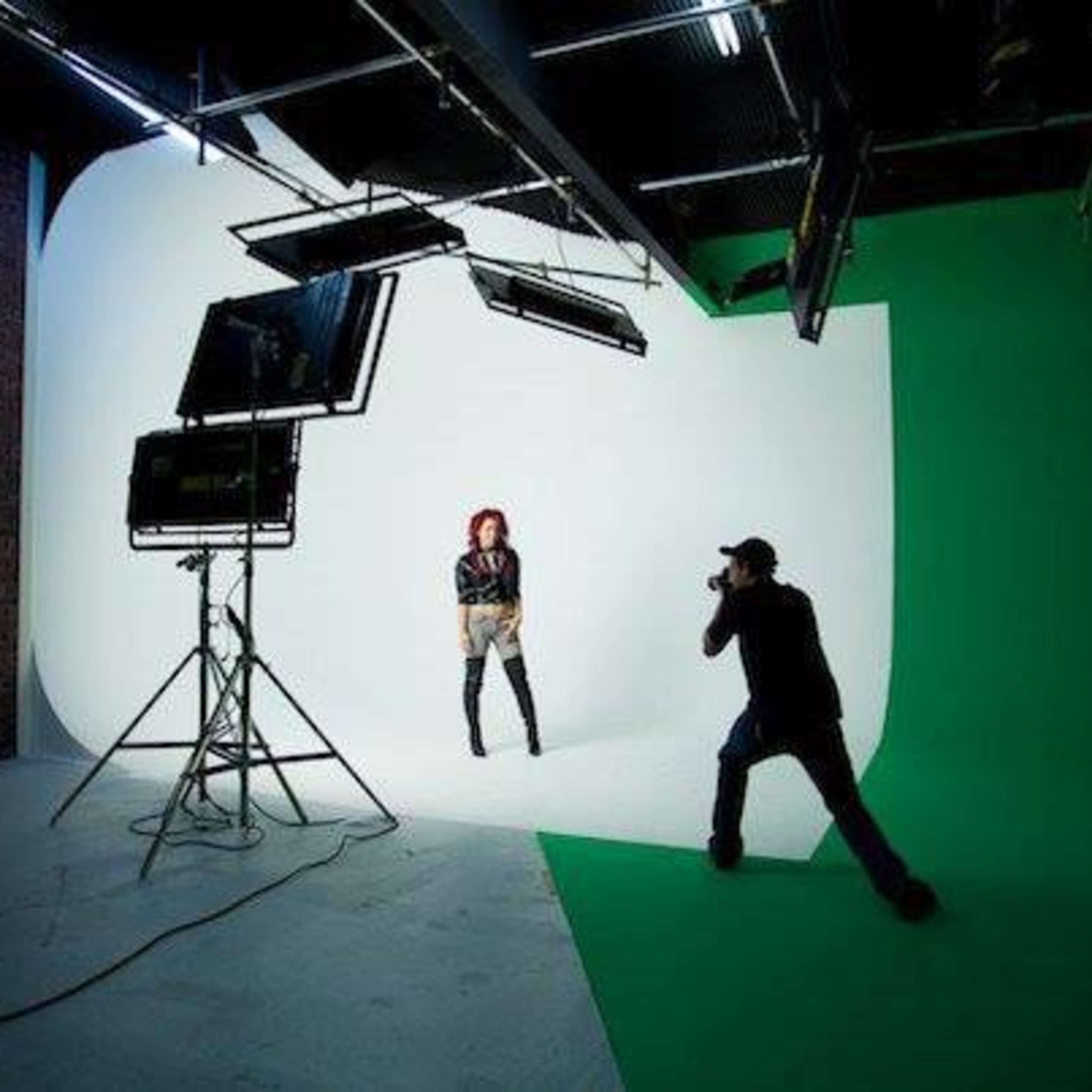 A photographer captures an image of a model posing in a studio with a green backdrop and multiple lighting setups.