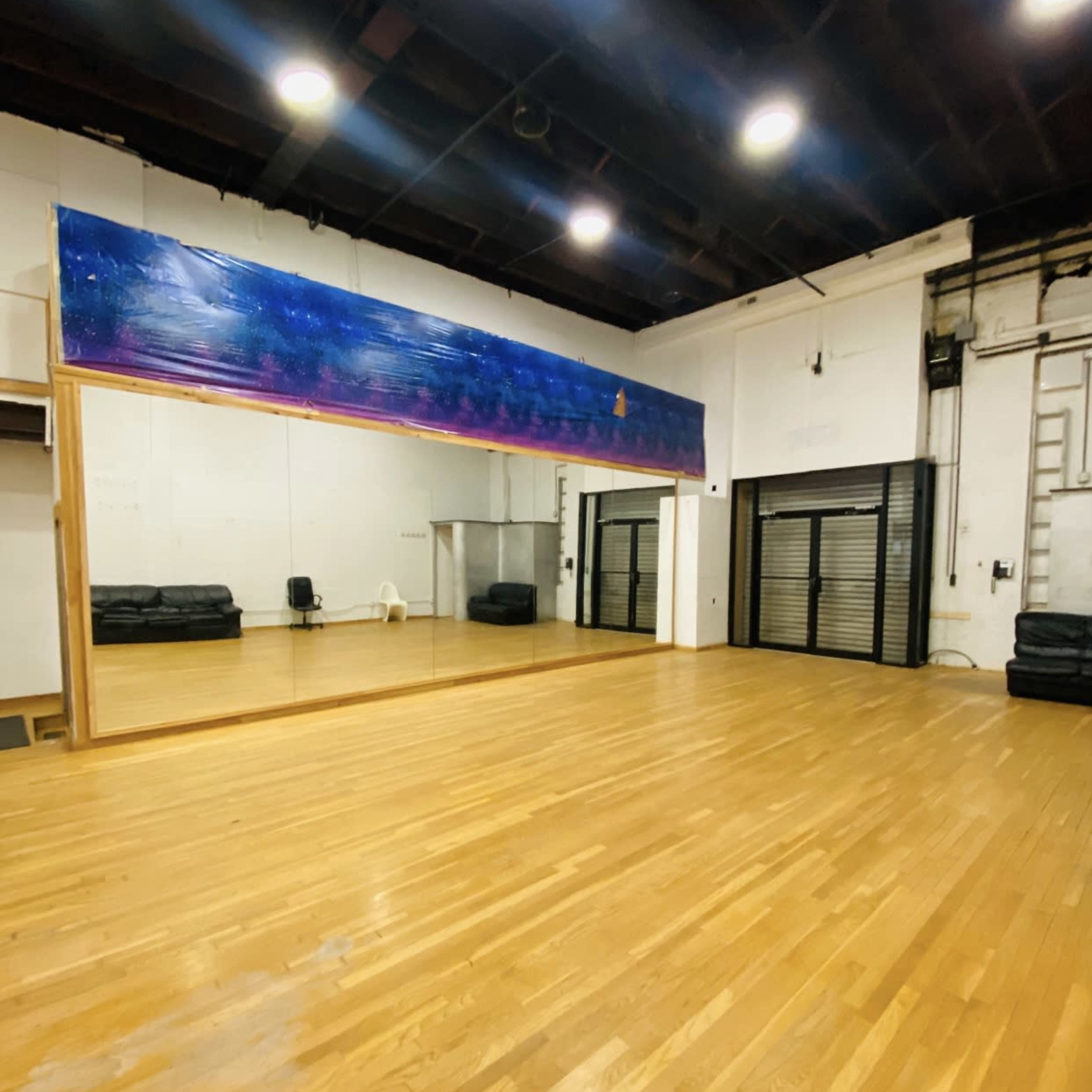 A spacious dance studio featuring a wooden floor, a large mirror, and a colorful mural along one wall.