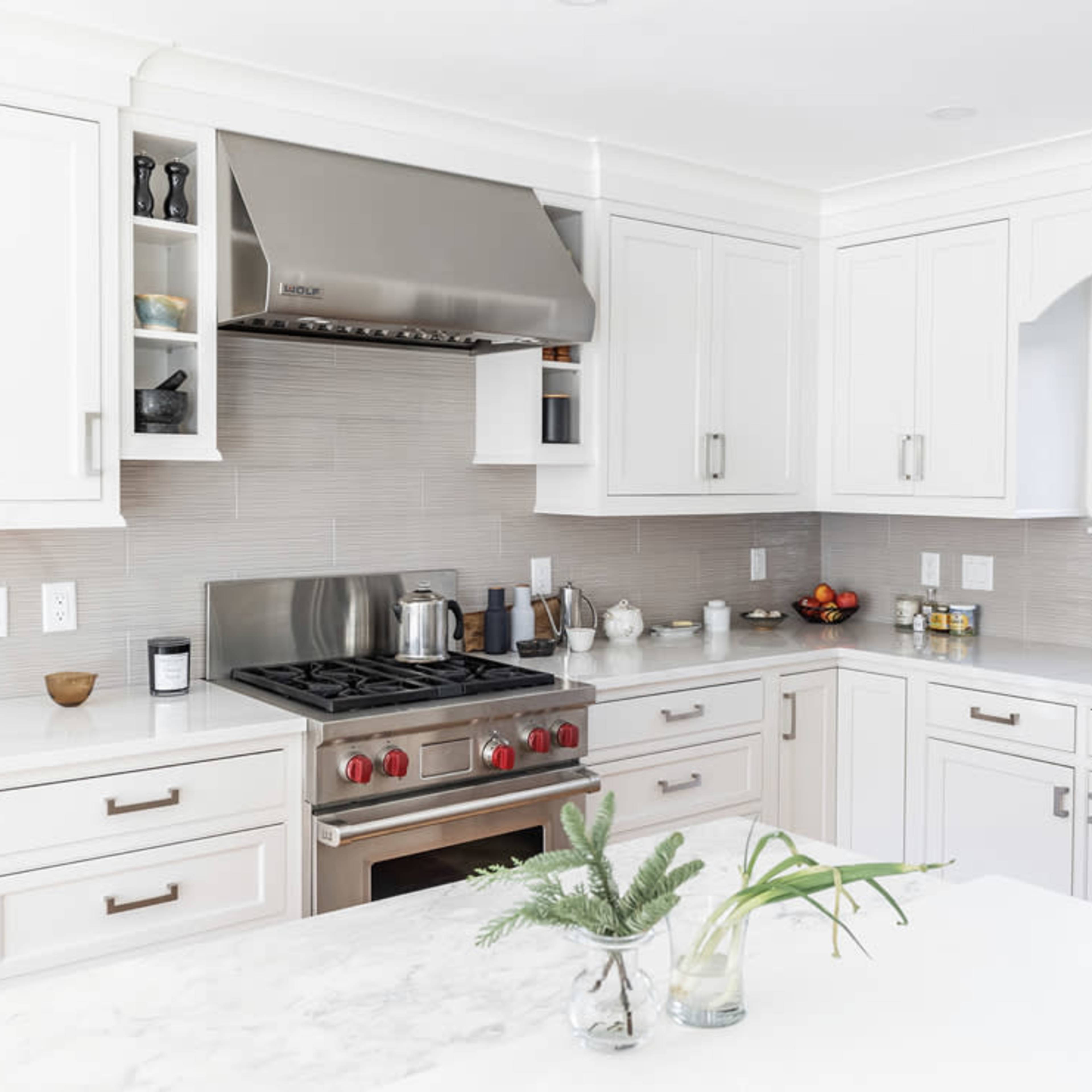 A modern kitchen features white cabinetry, a stainless steel refrigerator, and a gas stove beneath a metallic hood.
