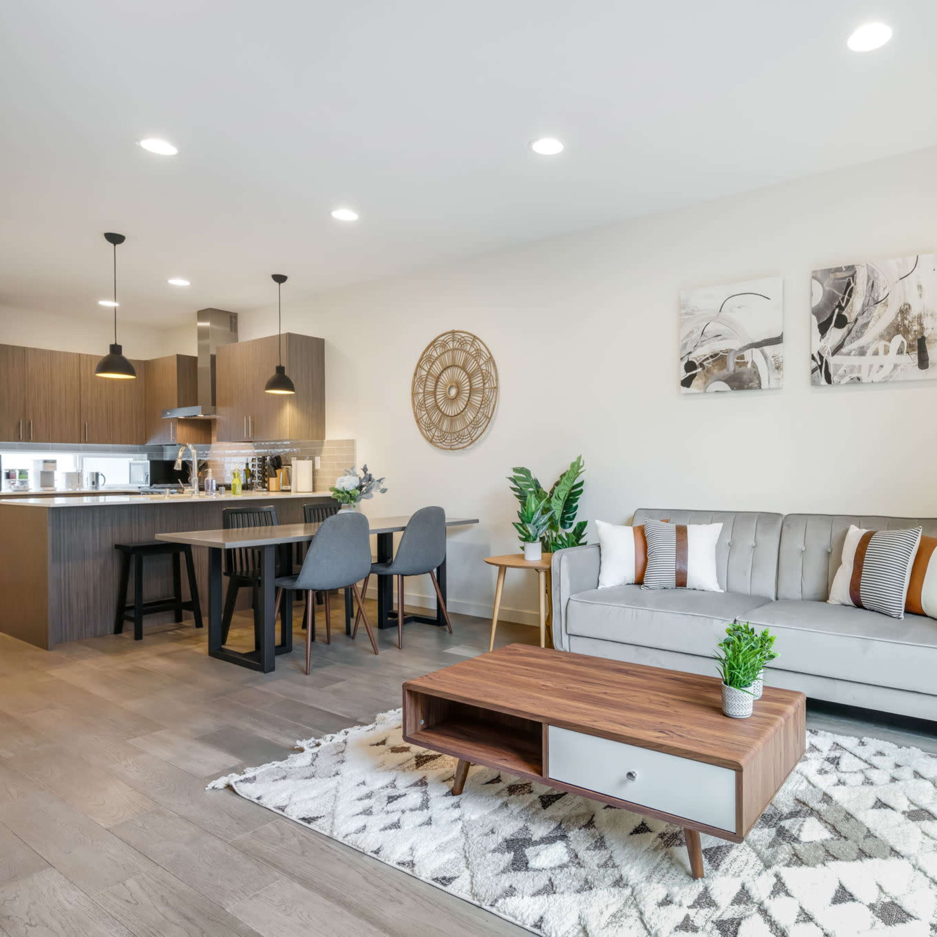 A modern open-concept living space with a dining area, kitchen, and a seating area featuring a sofa and a coffee table on a patterned rug.