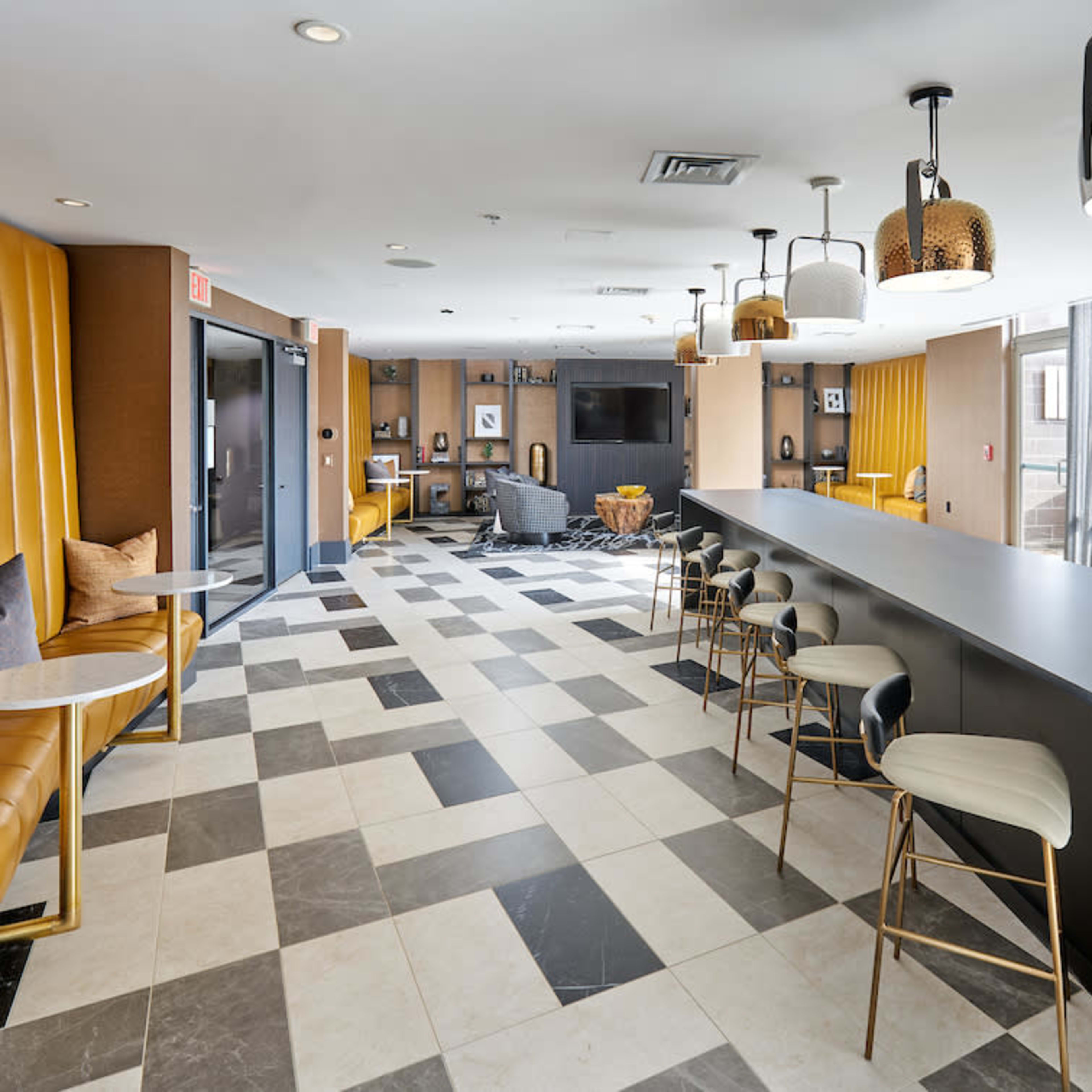 A modern lounge area featuring a long black bar counter, tan leather seating, and geometric tile flooring.