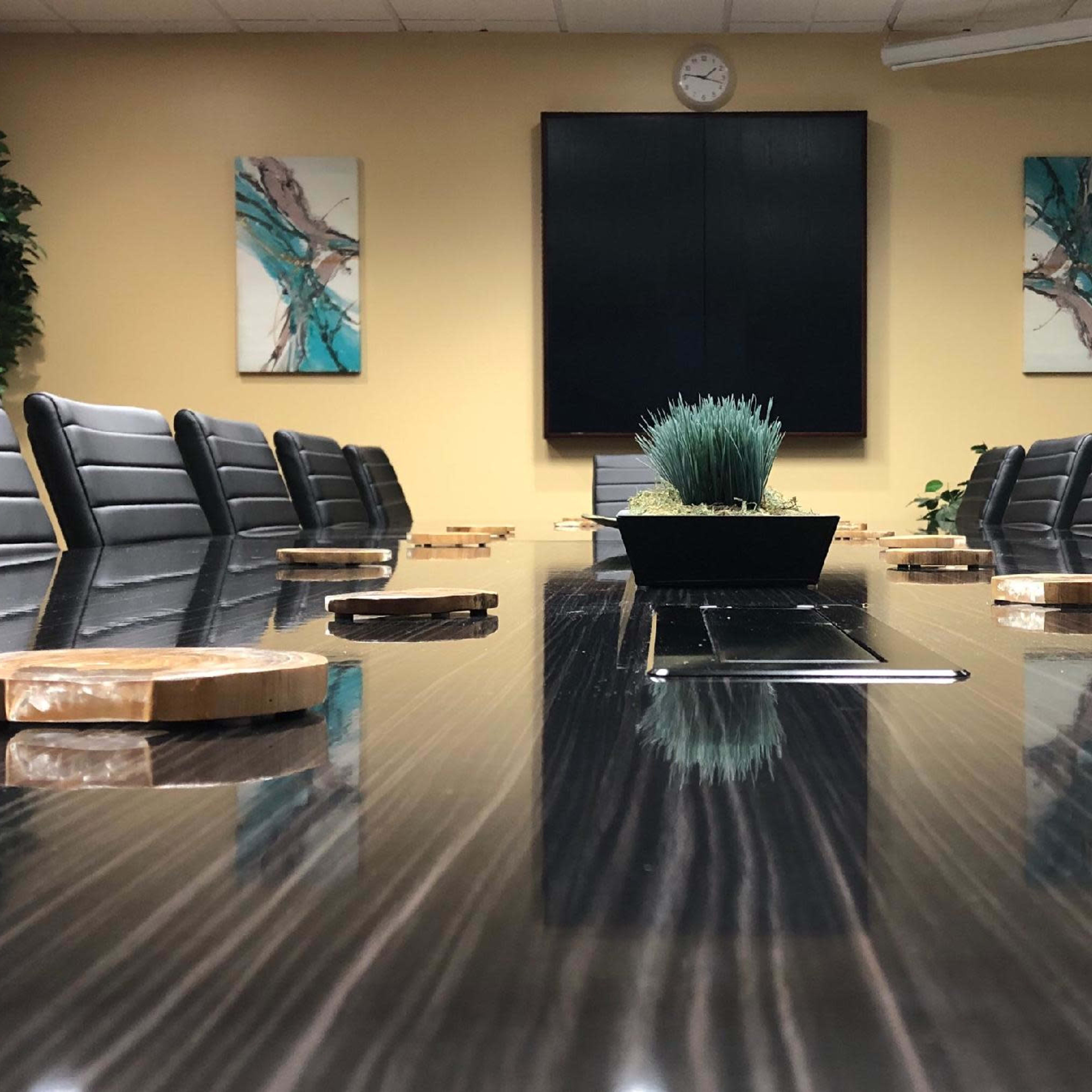 A modern conference room features a long table surrounded by black leather chairs, with a plant centerpiece on the table and abstract artwork on the walls.