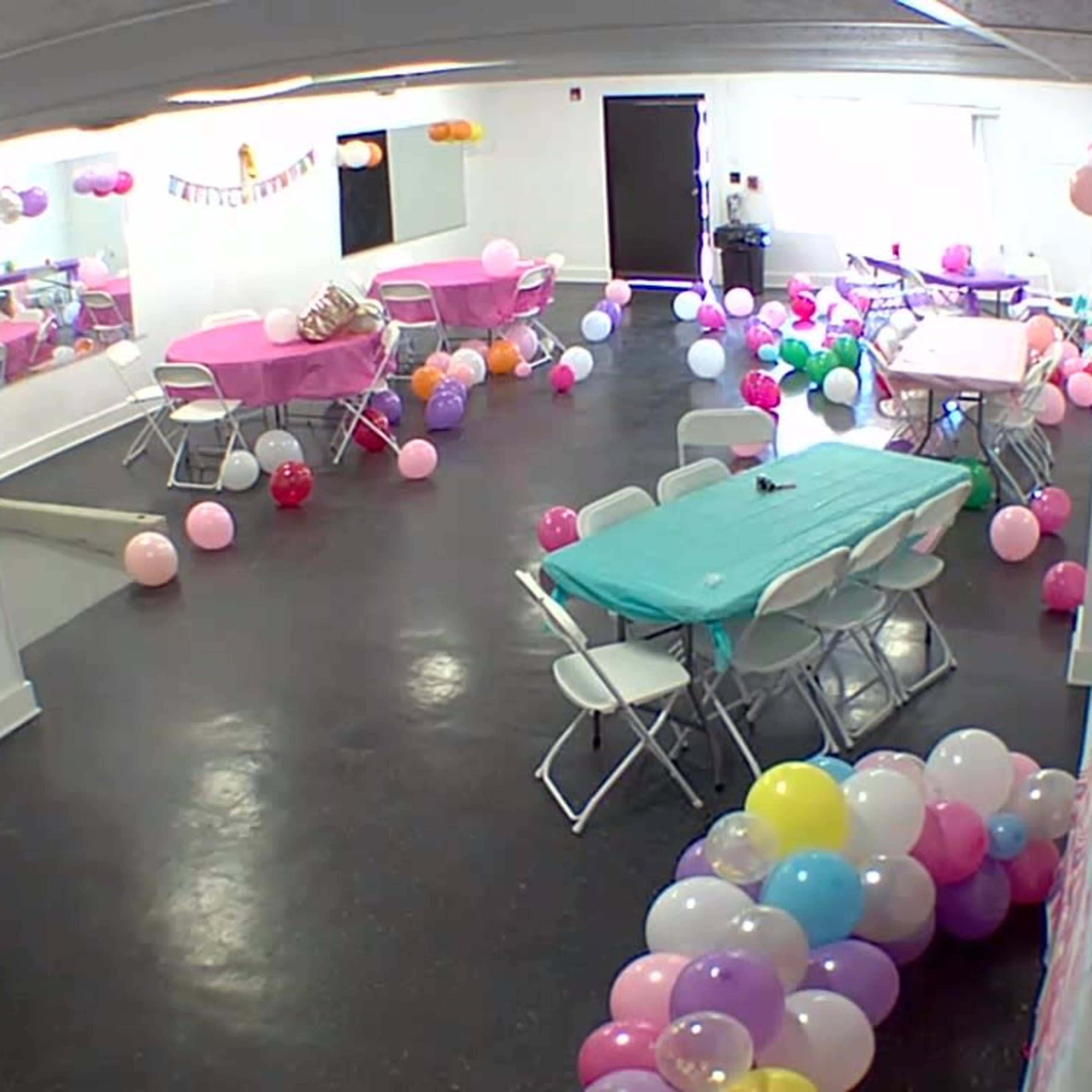 A decorated party room with tables set up, colorful balloons scattered across the floor, and a festive atmosphere.