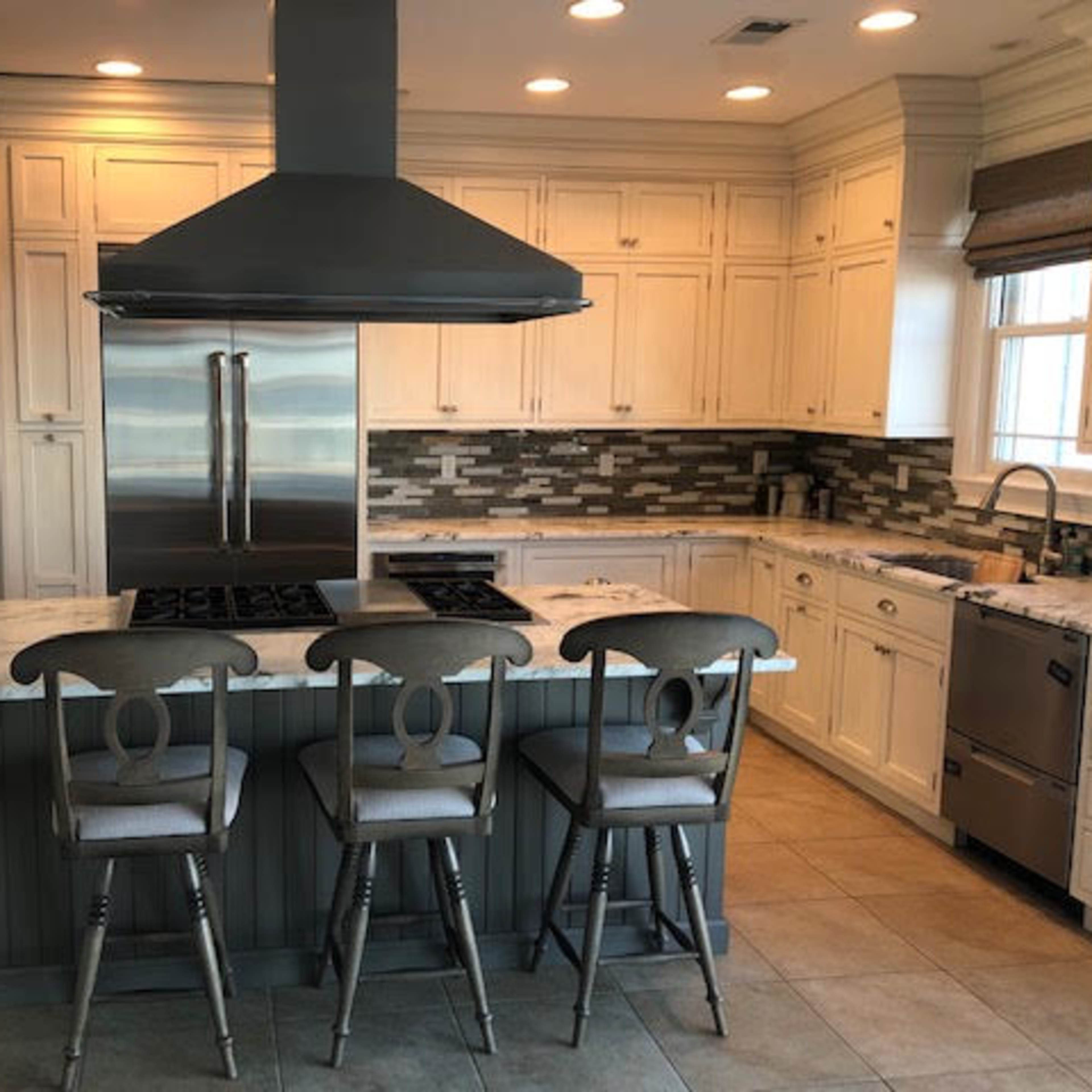 A modern kitchen with white cabinets, a central island with four bar stools, and stainless steel appliances.