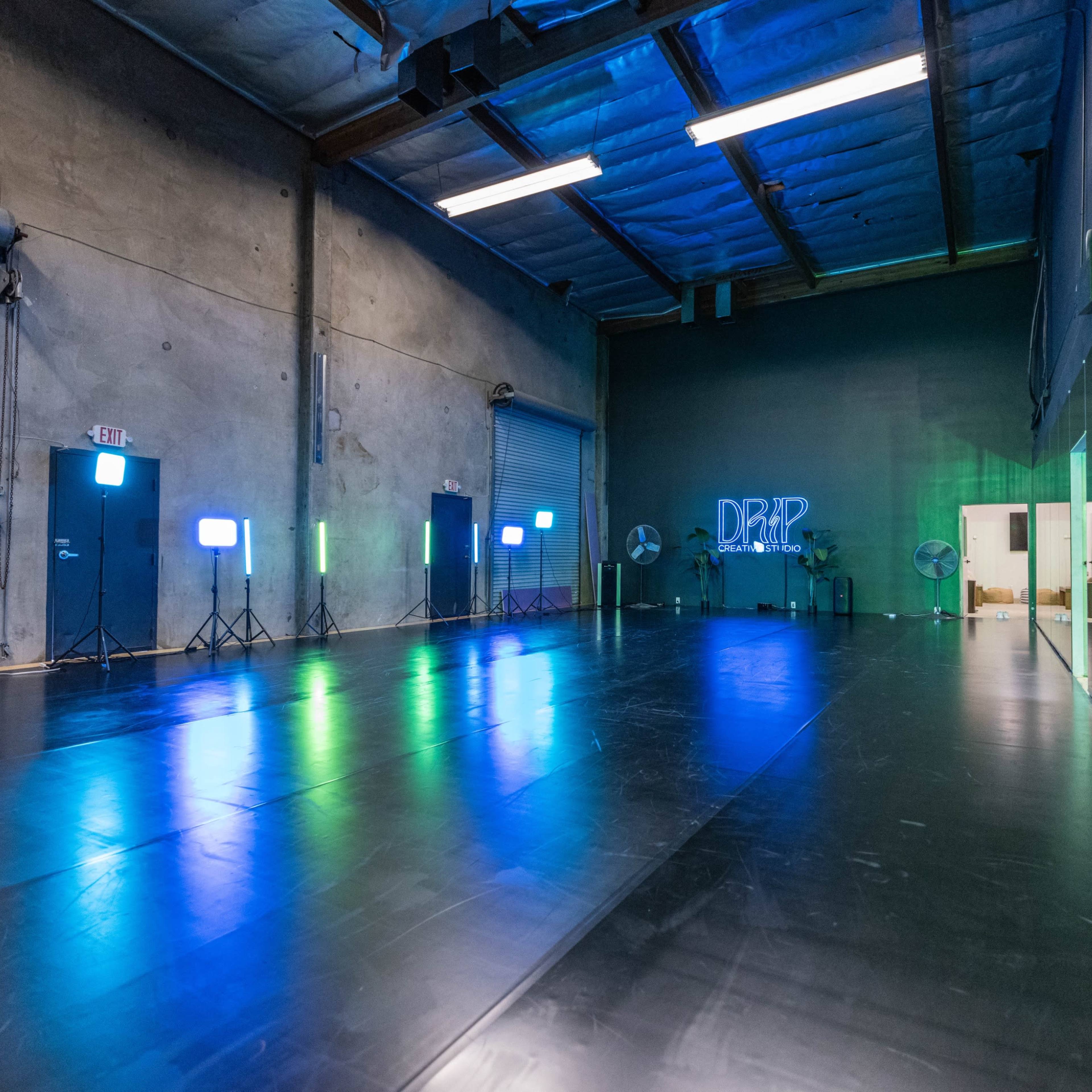 A spacious, empty dance studio with a reflective floor, multiple lights on stands, and large mirrors along one wall.