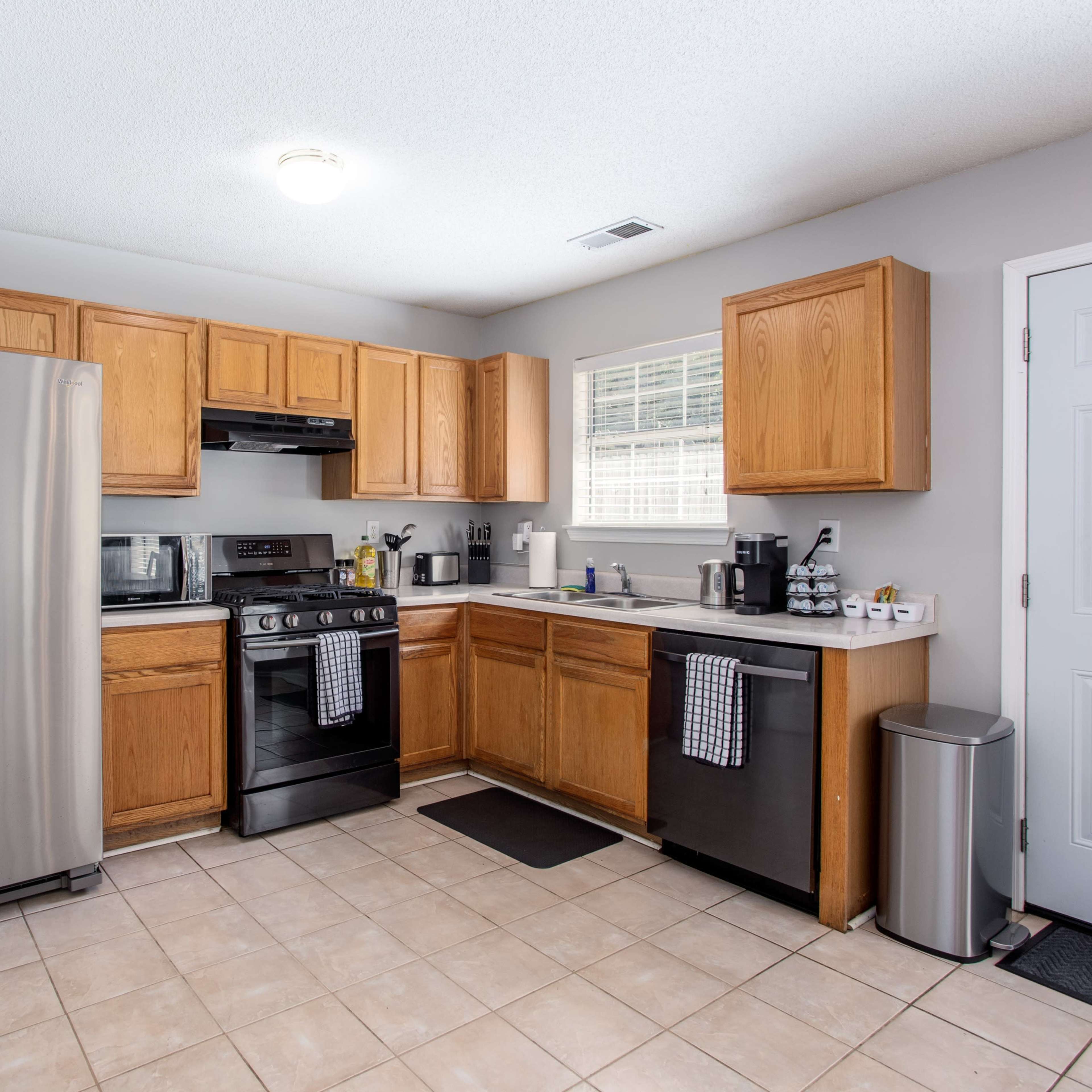 A modern kitchen with wooden cabinets, stainless steel appliances, and a tiled floor.