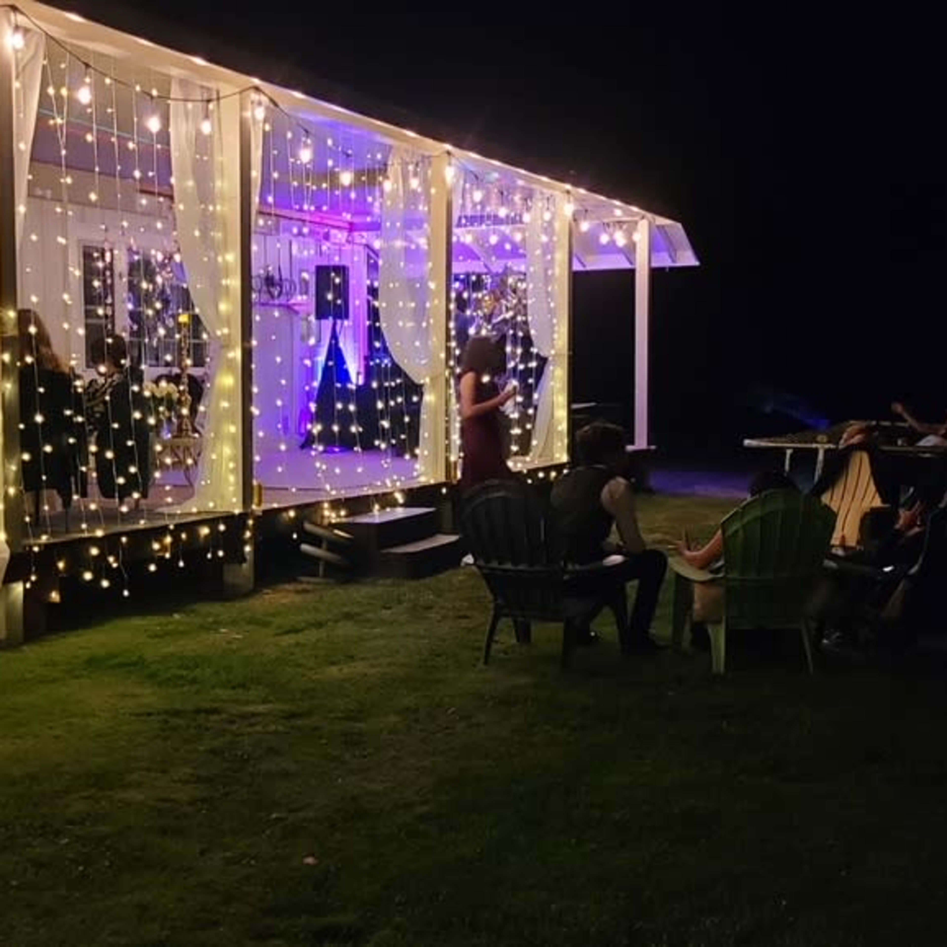 A decorated outdoor patio with string lights and people gathered around a table in the evening.