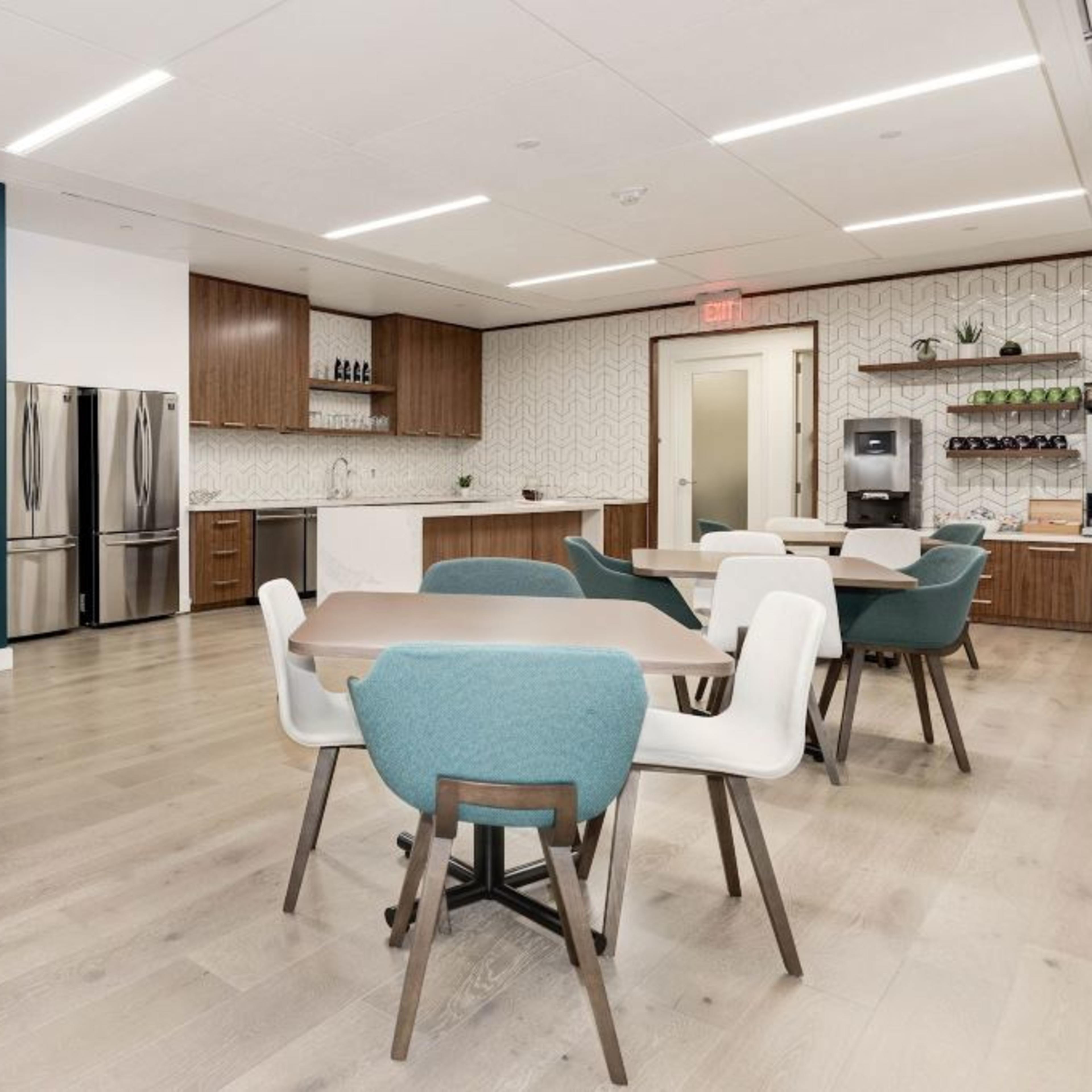 A modern break room with seating areas, appliances, and a decorative wall featuring a photo of an outdoor scene.