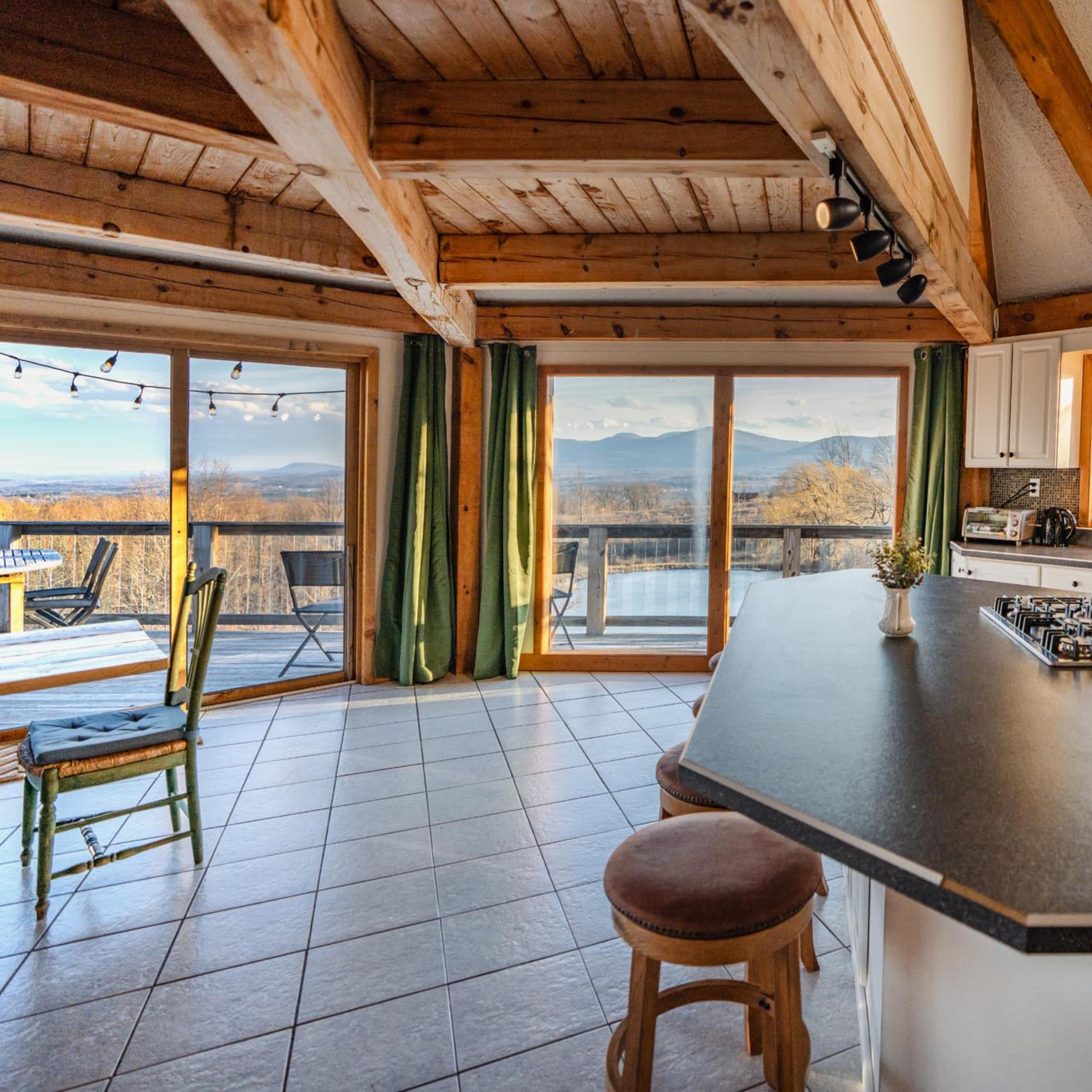 A spacious kitchen features a central island with a stovetop and has large windows that offer a view of the surrounding mountains.