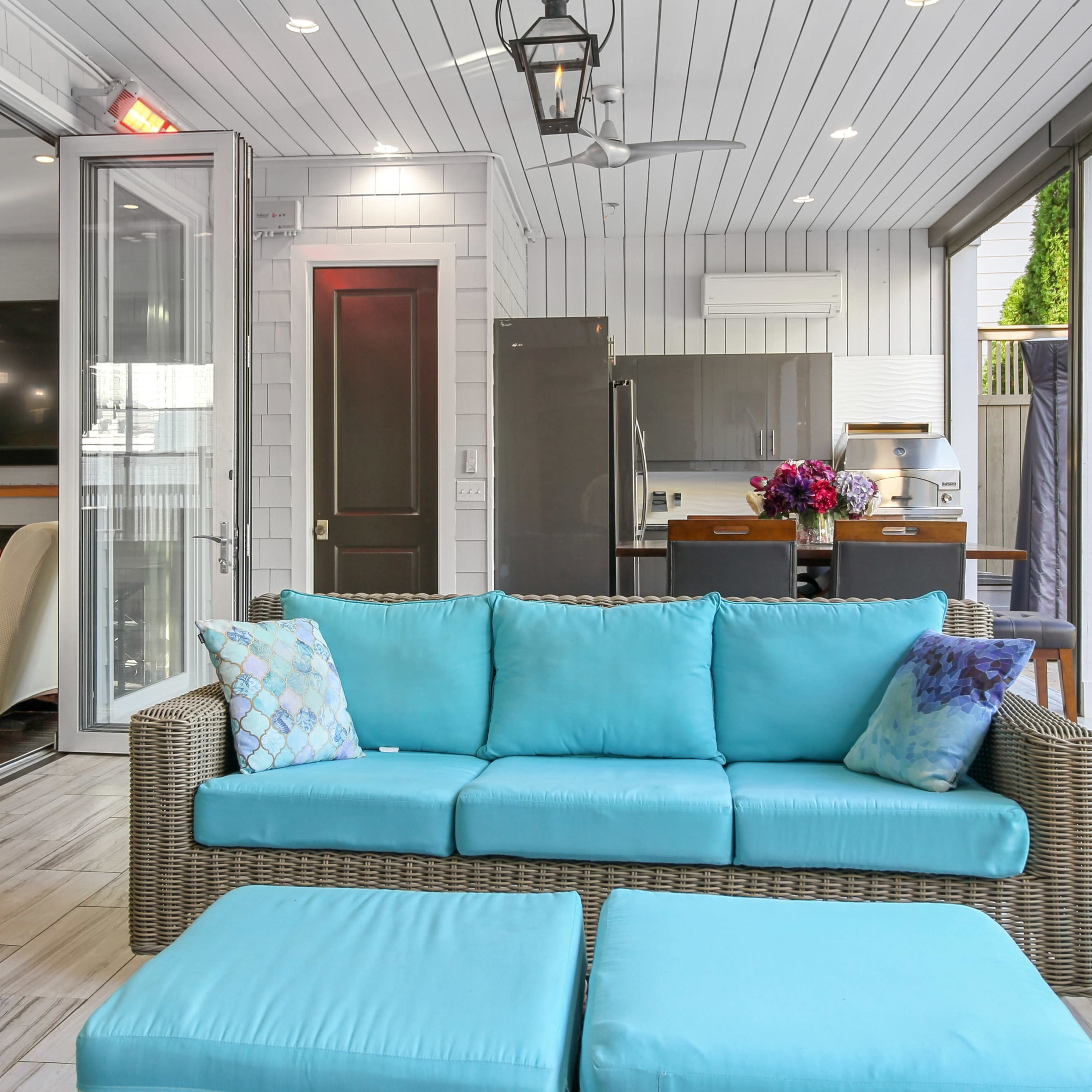 A modern indoor-outdoor living space featuring a turquoise sofa, a kitchen area, and large glass doors opening to a patio.