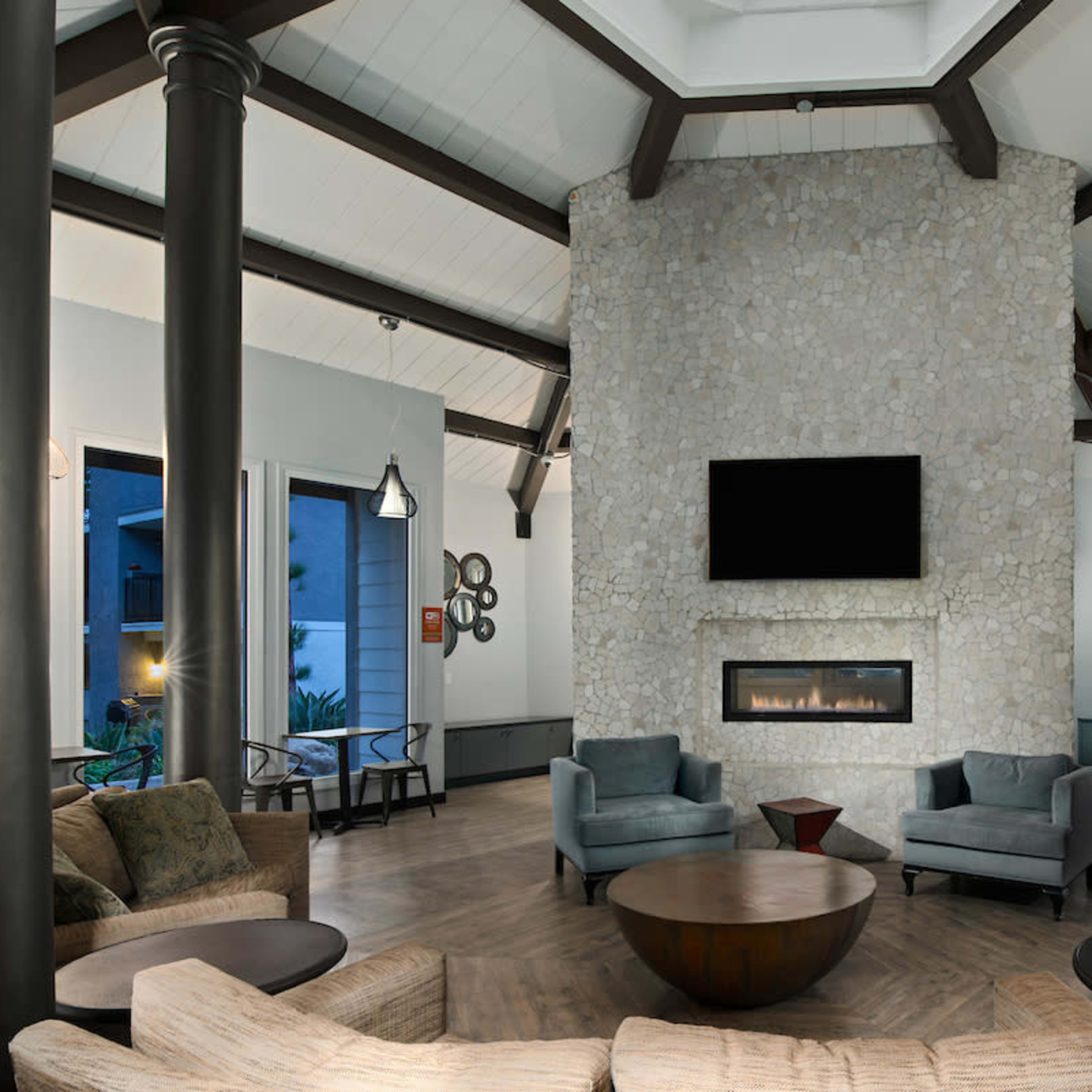 A modern living space with a stone fireplace as the focal point, surrounded by seating arrangements and large windows.
