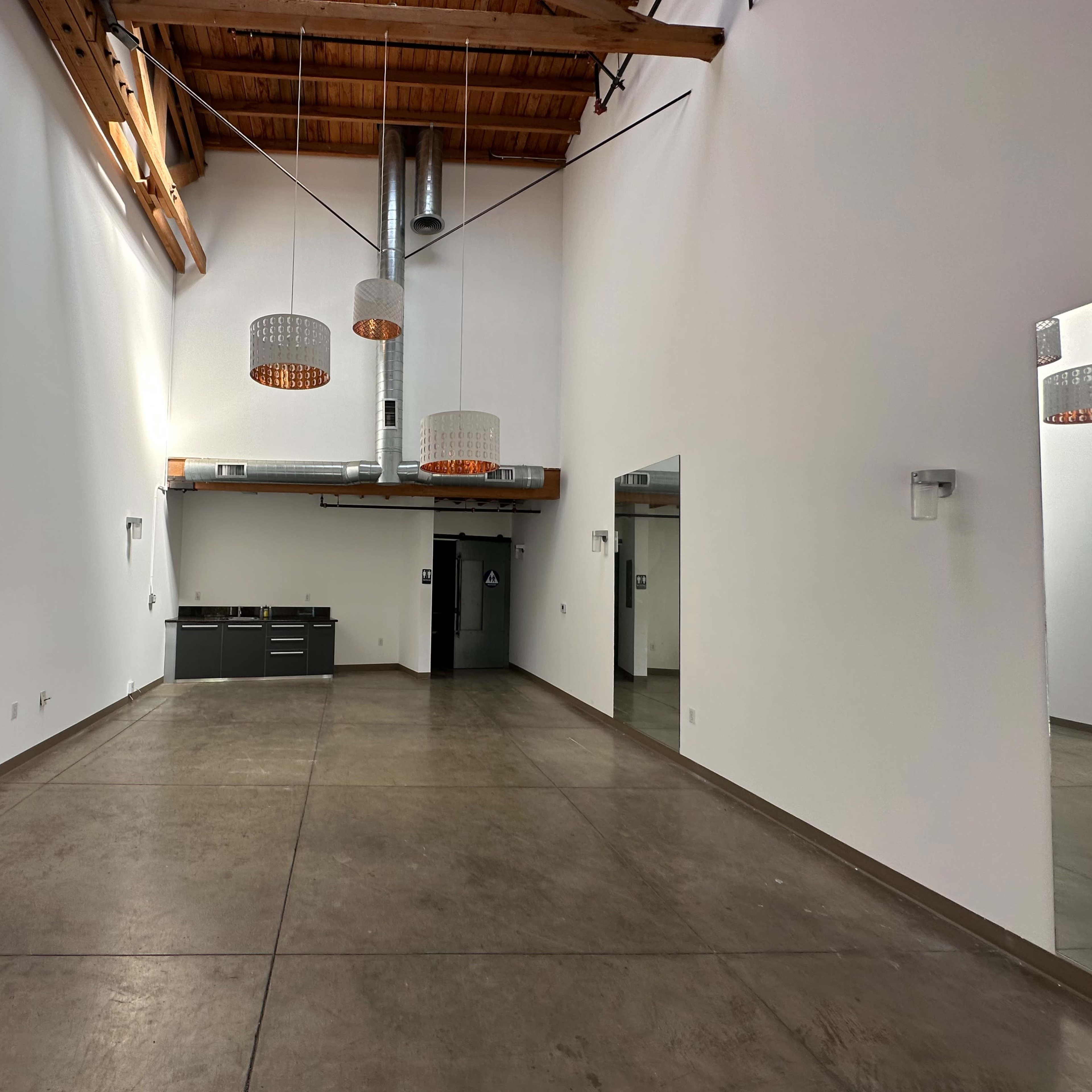 A spacious interior with high ceilings, exposed wooden beams, concrete floors, and minimalist lighting fixtures.