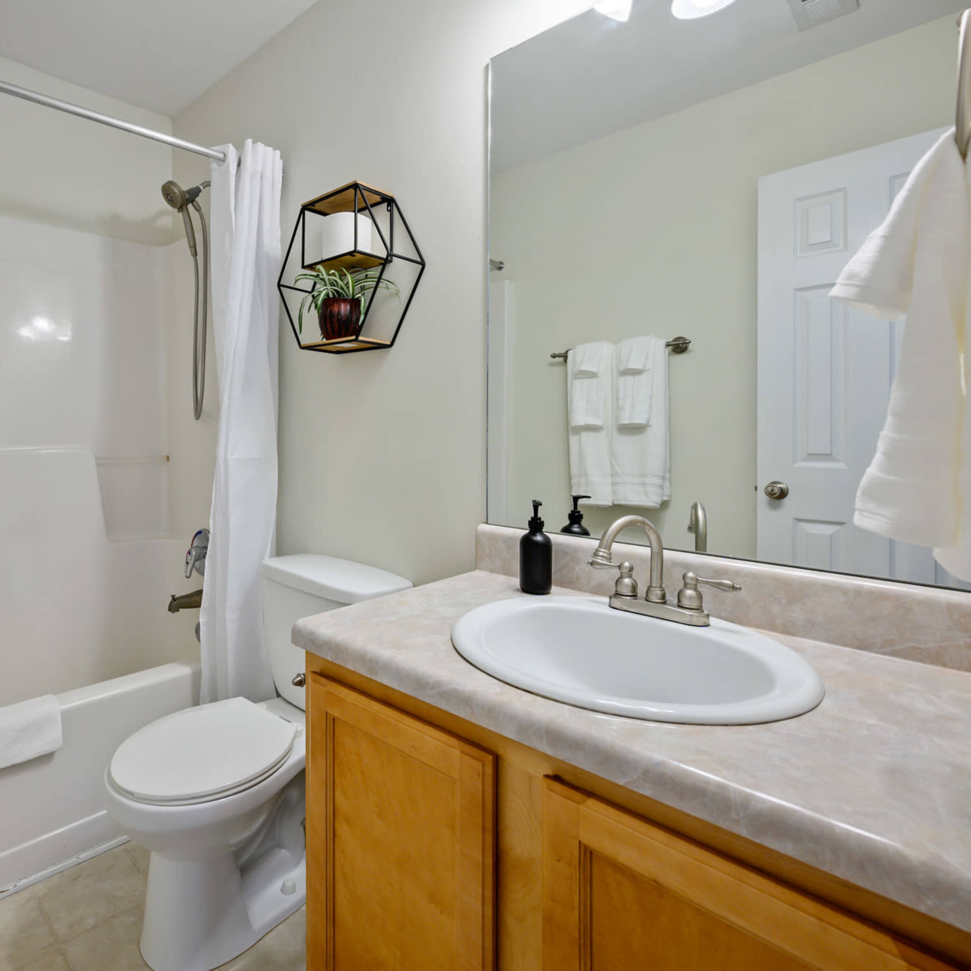 A clean bathroom featuring a bathtub with a shower curtain, a toilet, a sink with a countertop, and a mirror, along with neatly arranged towels.