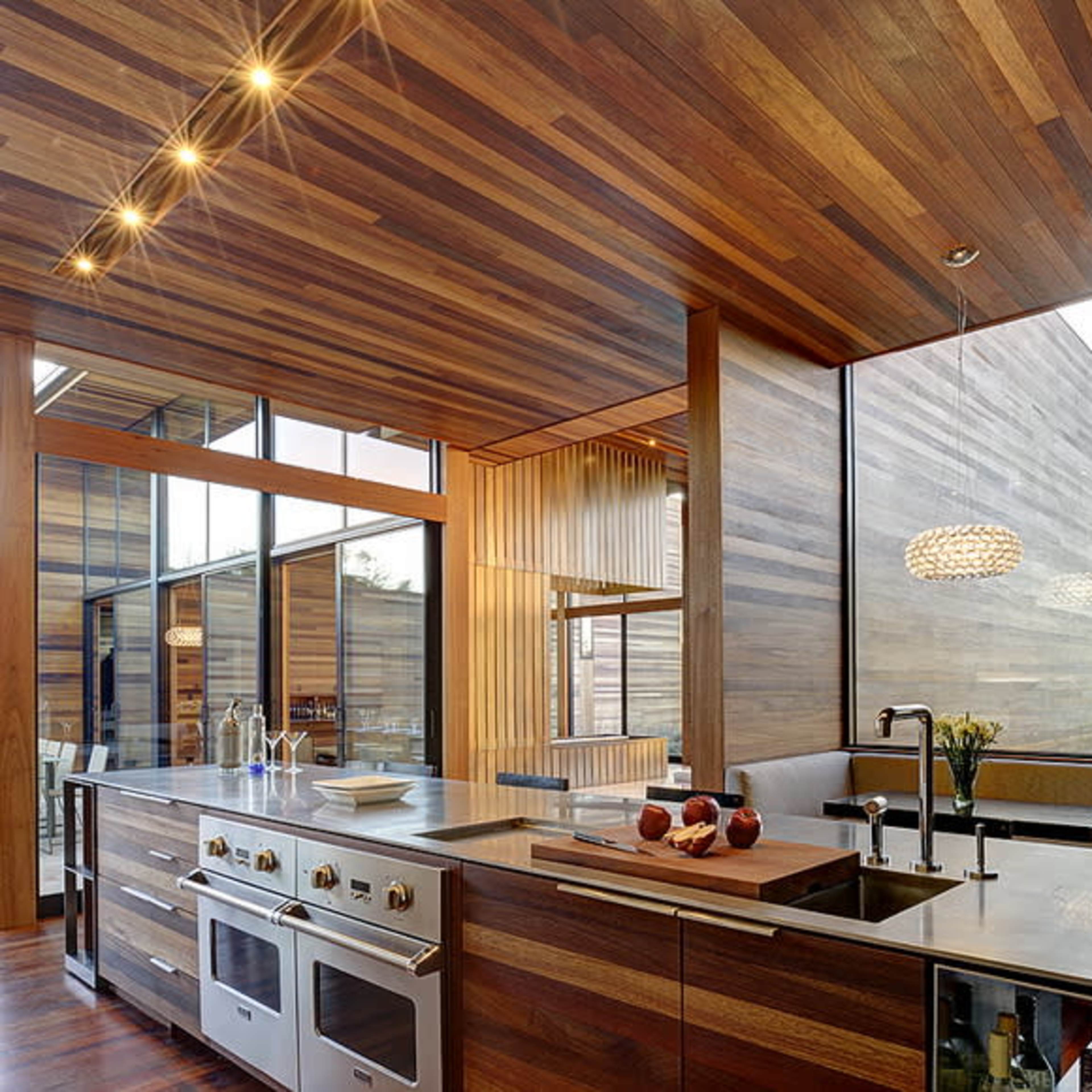 The kitchen features a modern design with wooden walls and ceiling, large windows, and stainless steel appliances.