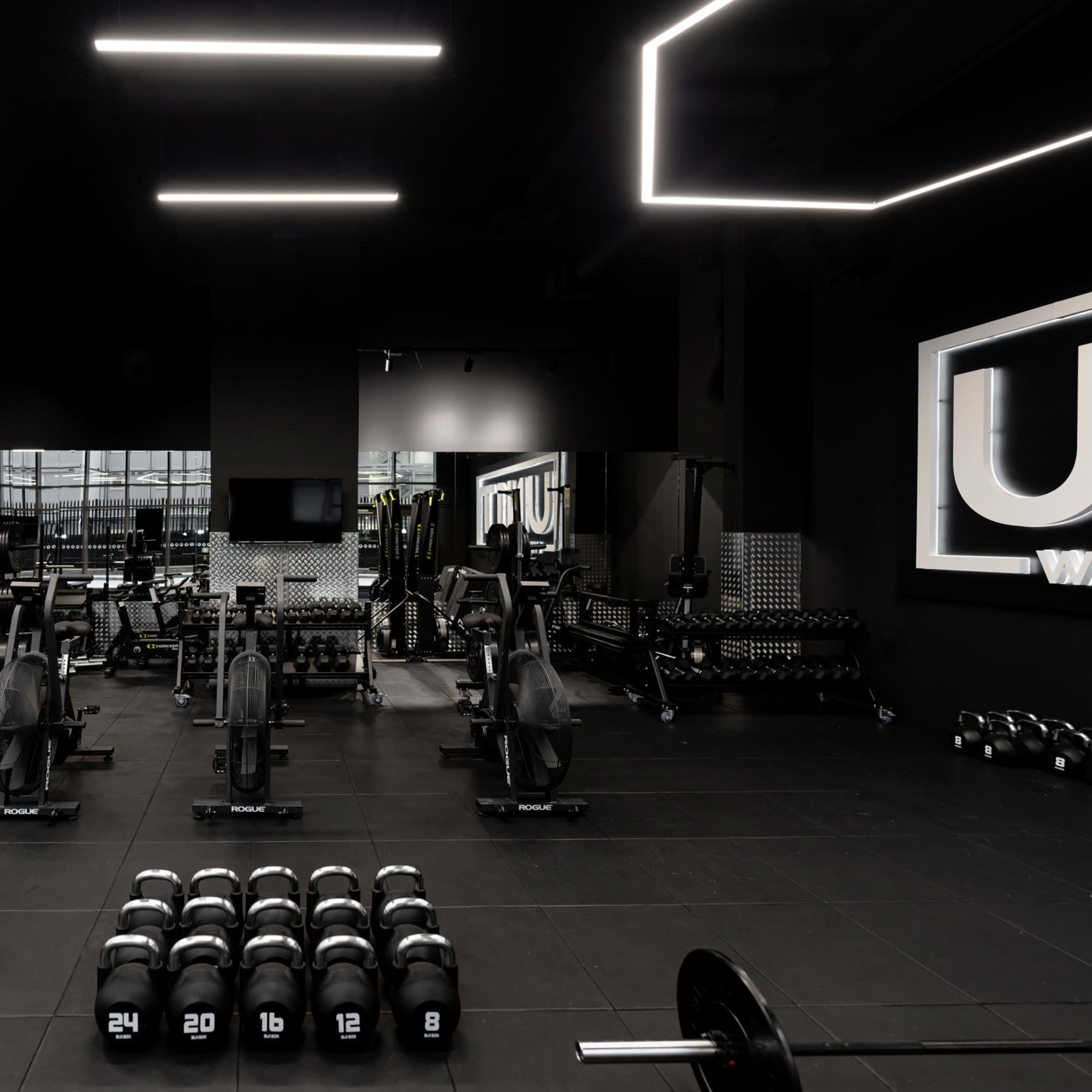 A modern gym interior equipped with various weightlifting equipment, including dumbbells and rowing machines, under bright ceiling lights.