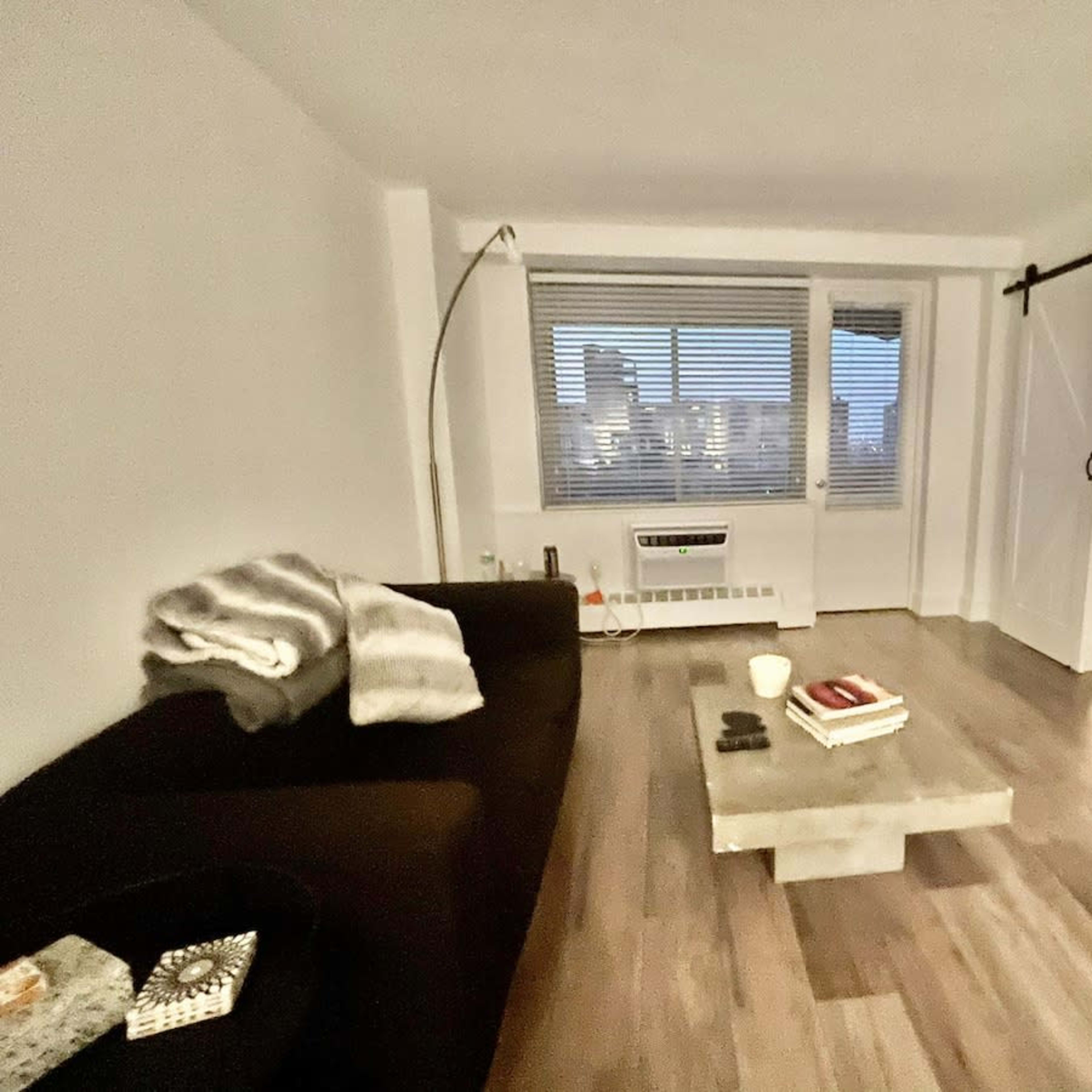 A modern living space features a dark sofa, a coffee table with books, and large windows overlooking a city skyline.