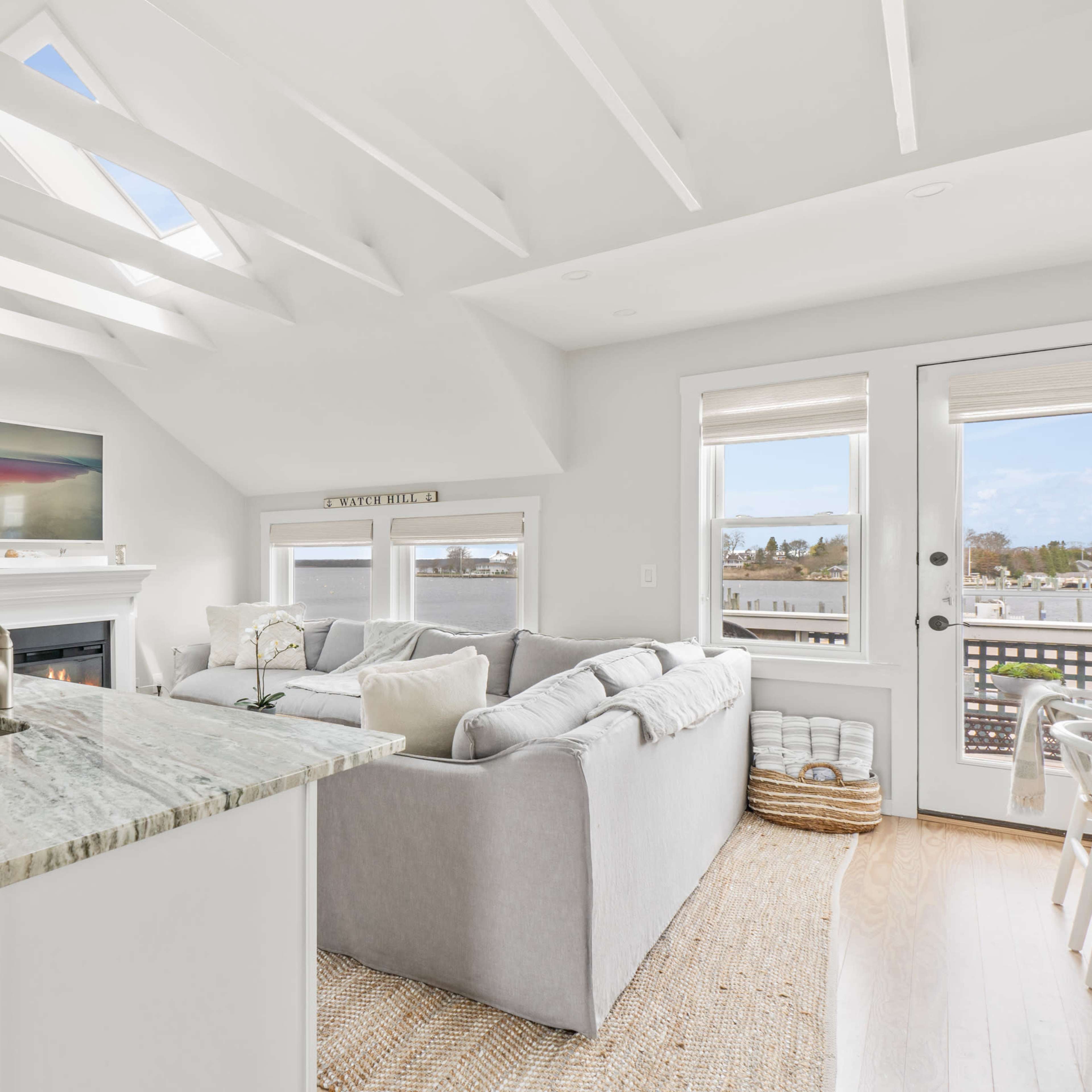 A bright living room with a fireplace, a large sectional sofa, and an open kitchen with a granite countertop.