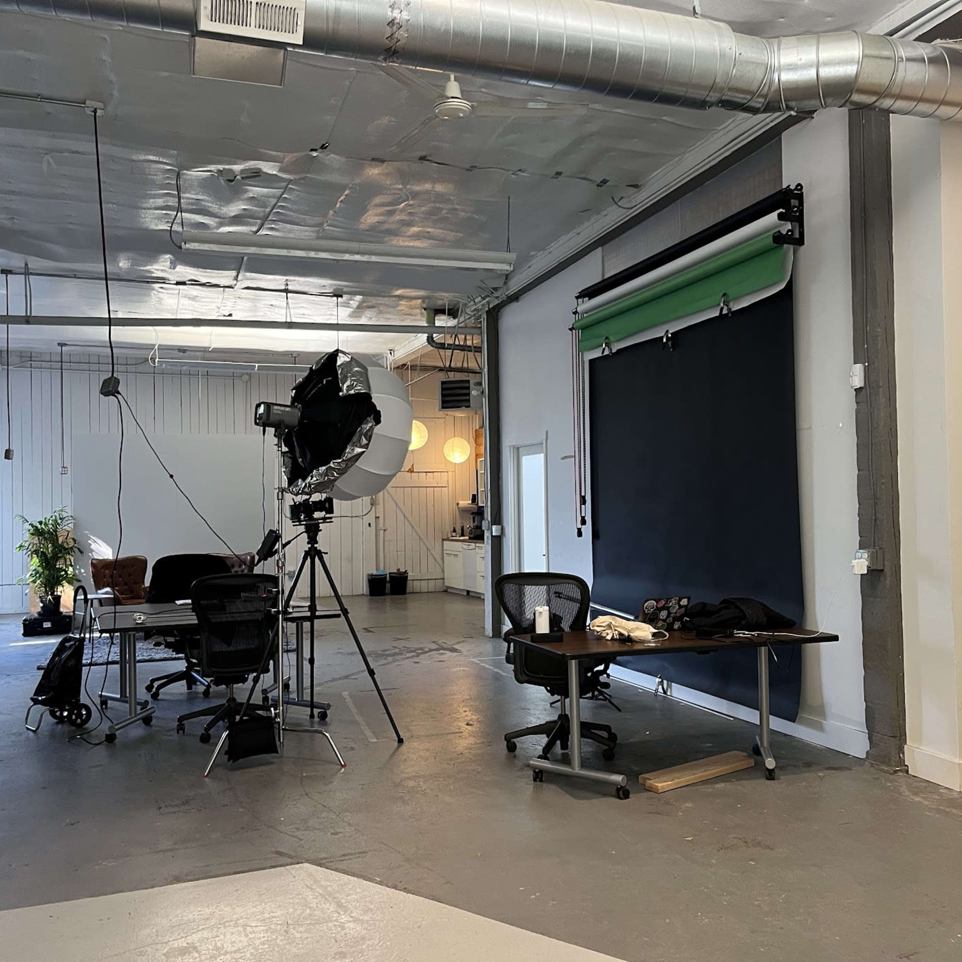 A large, well-lit studio space with a black backdrop, photography equipment, a desk, and a chair.