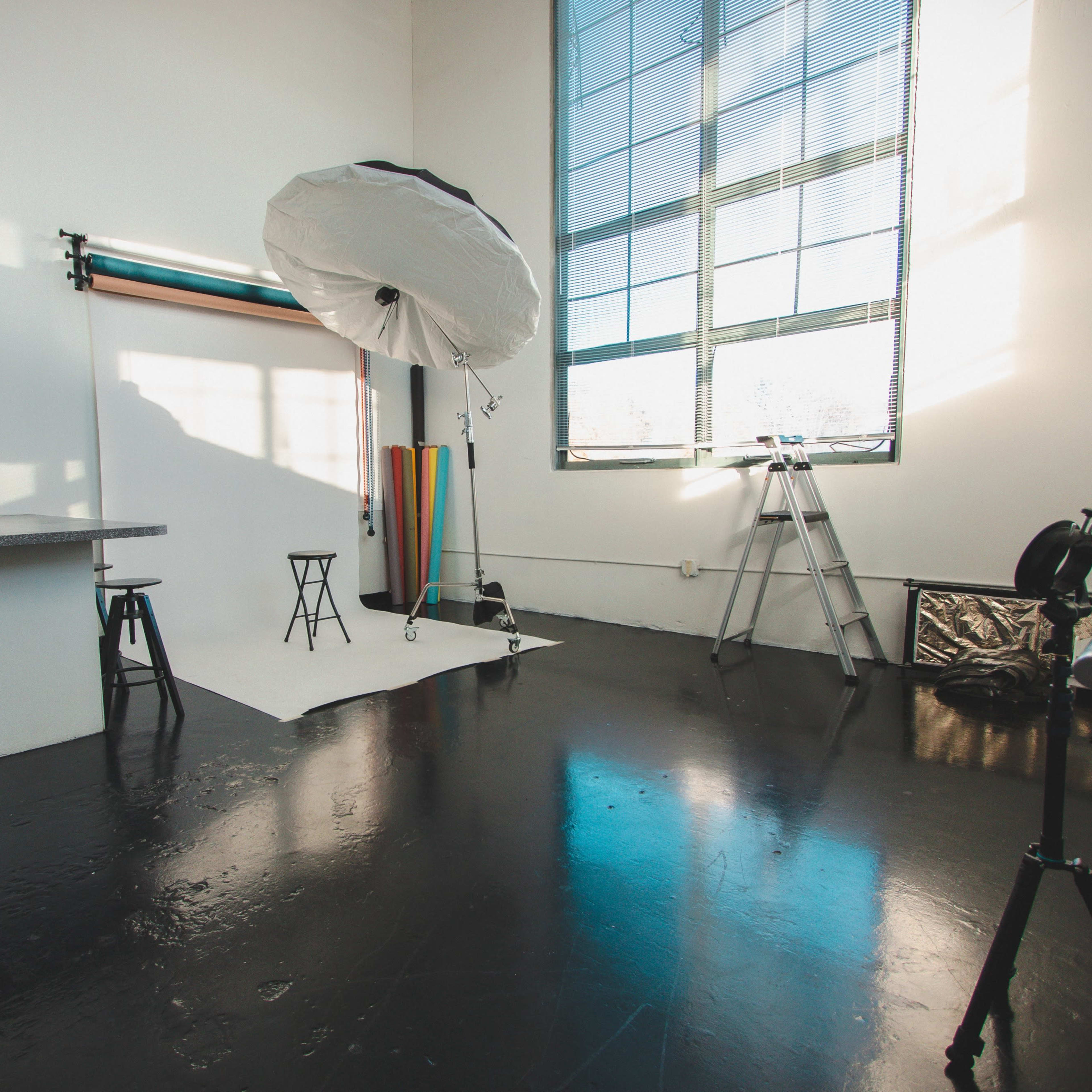 A well-lit photography studio featuring a backdrop, lighting equipment, and a ladder against the wall.