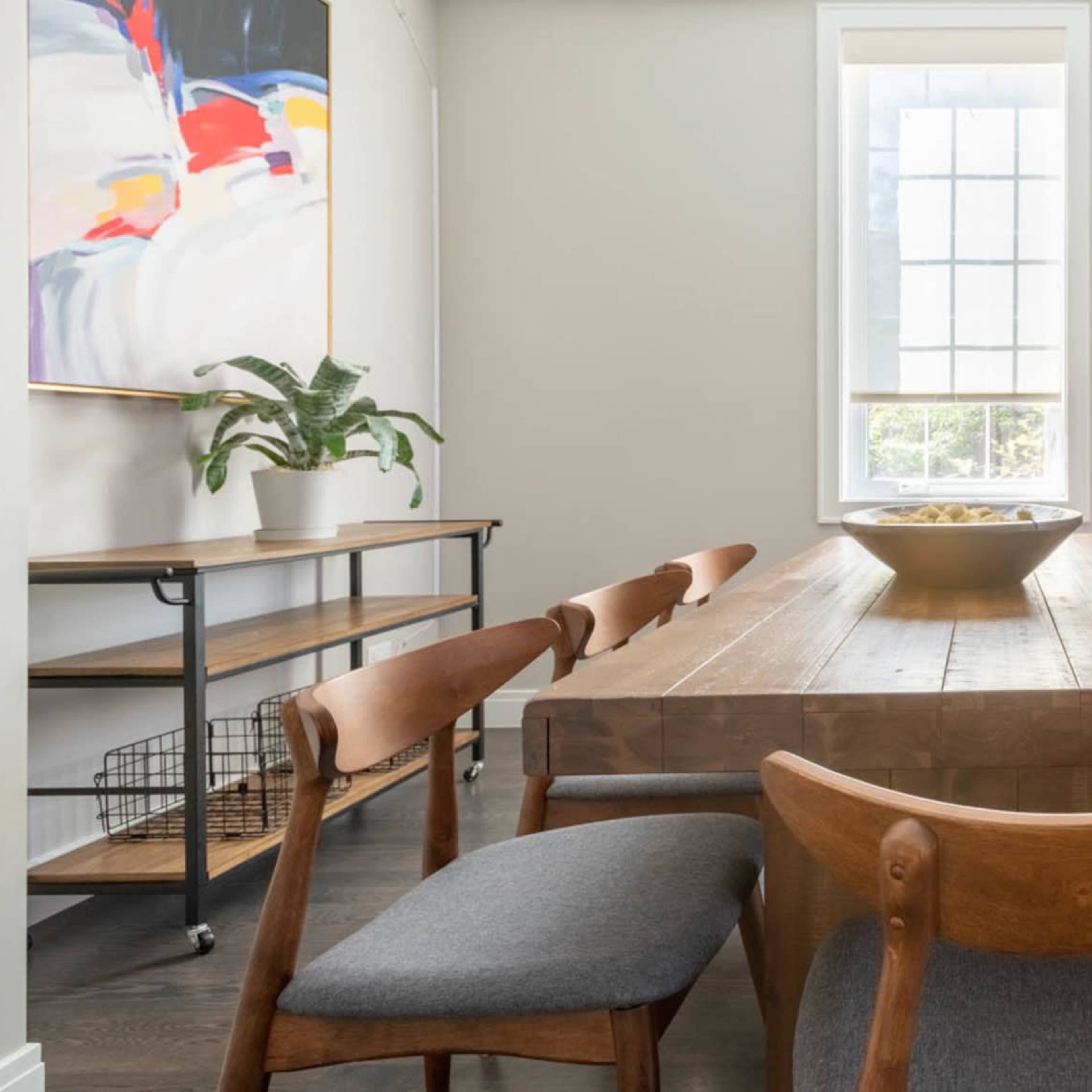 A dining area with a wooden table, several chairs, and a large window allowing natural light to enter.