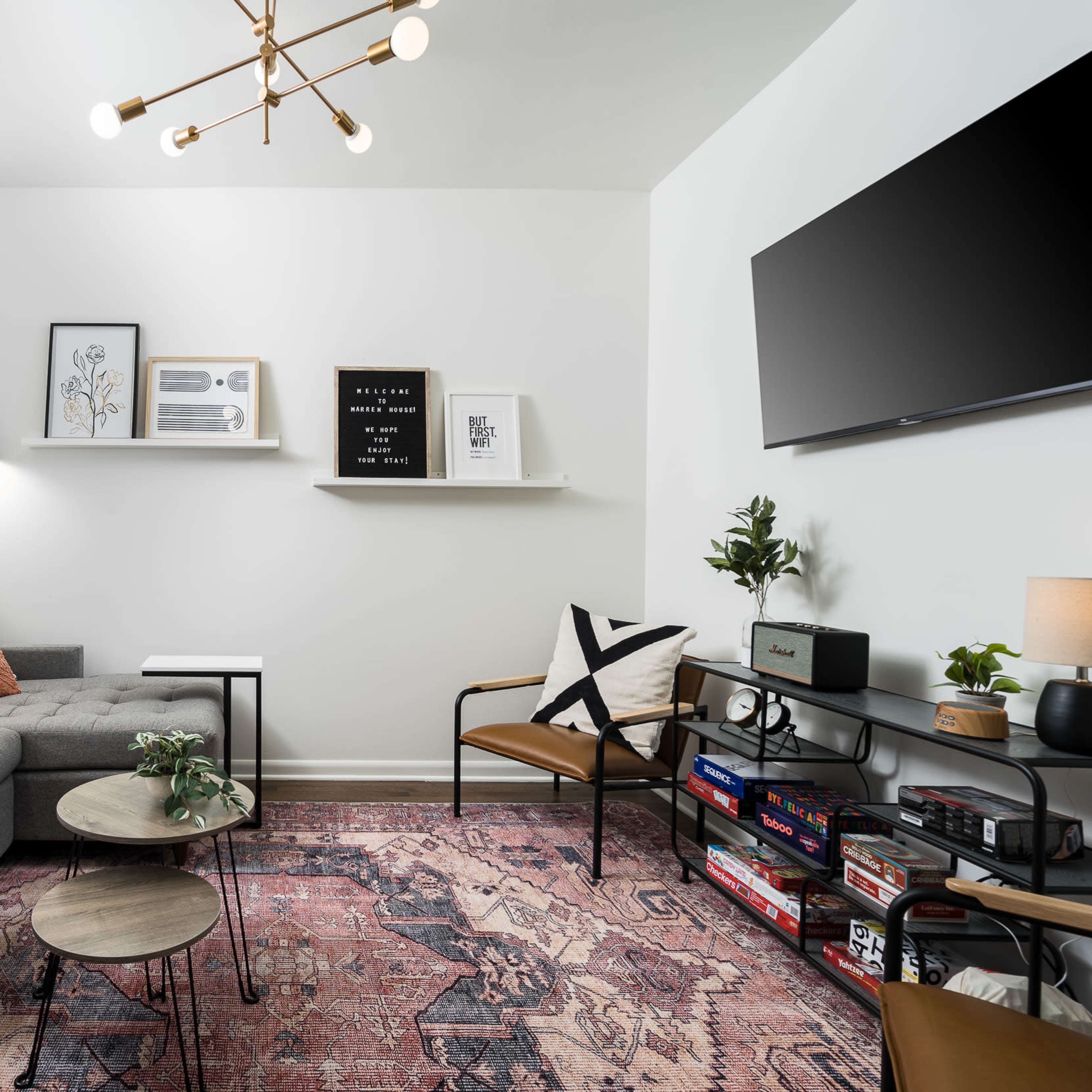 A modern living room features a gray sofa, a two-tiered coffee table, decorative wall art, and a television mounted on a white wall.