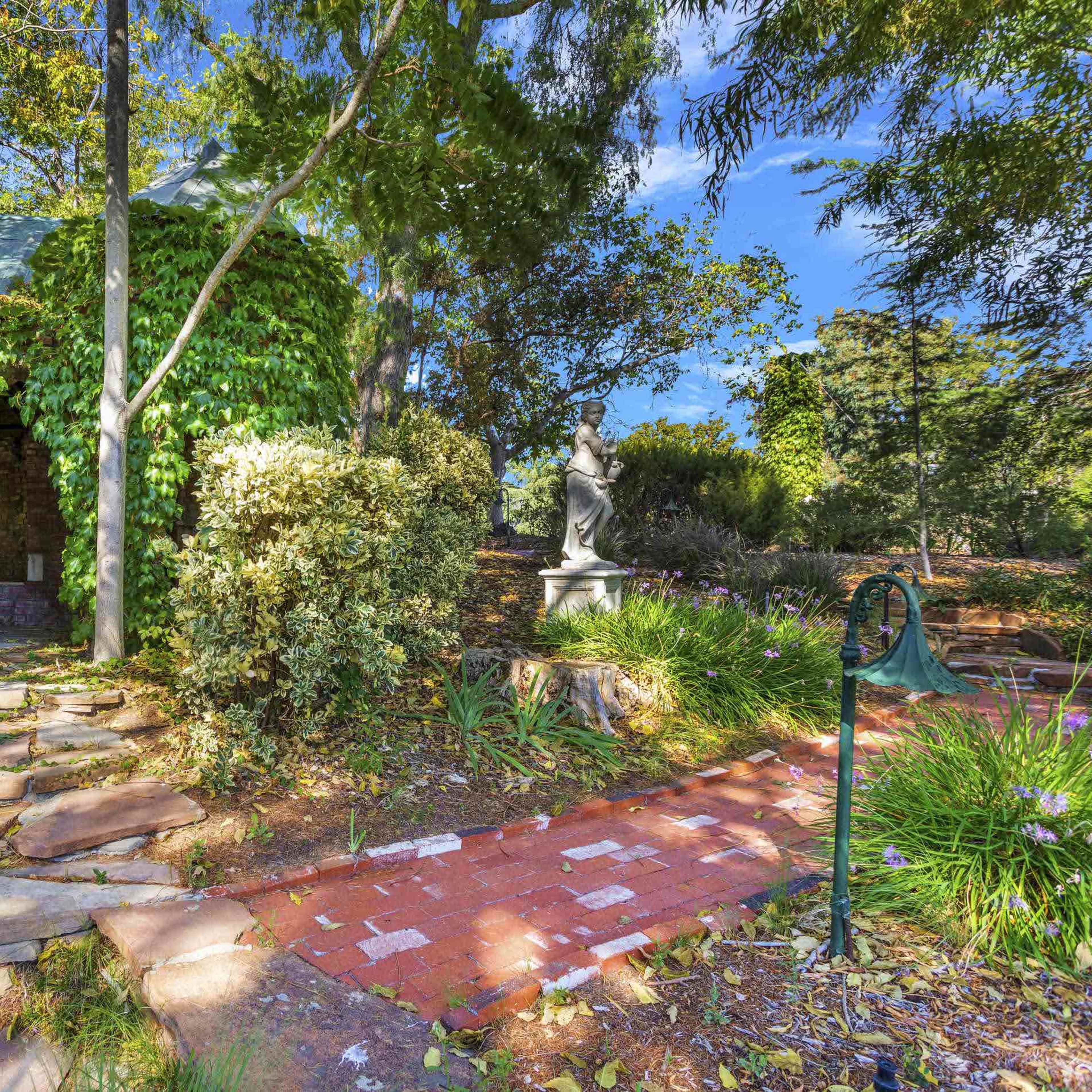 A stone pathway leads to a small, ivy-covered structure surrounded by trees and colorful foliage.