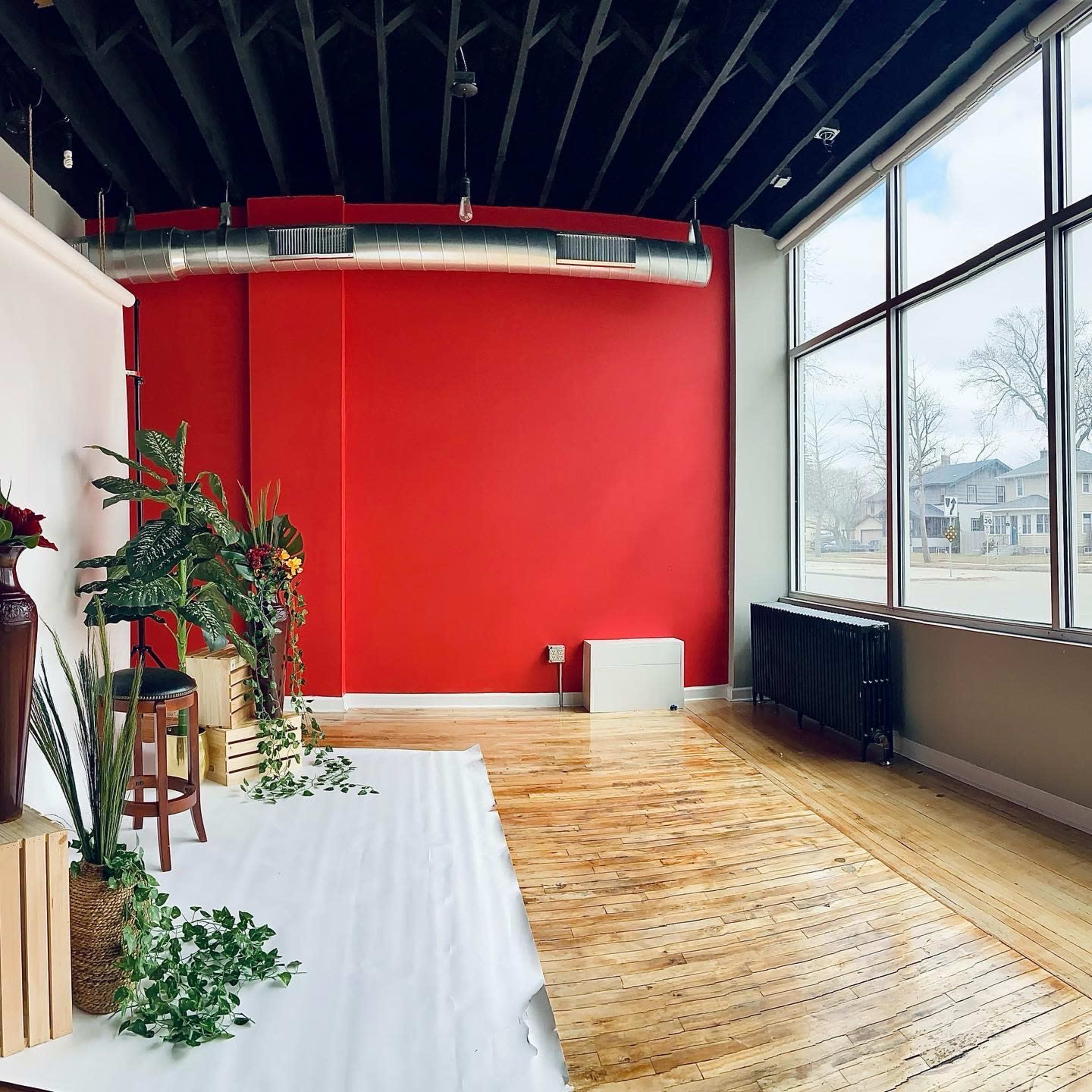 A spacious interior with a red accent wall, wooden floors, and large windows allowing natural light to enter.