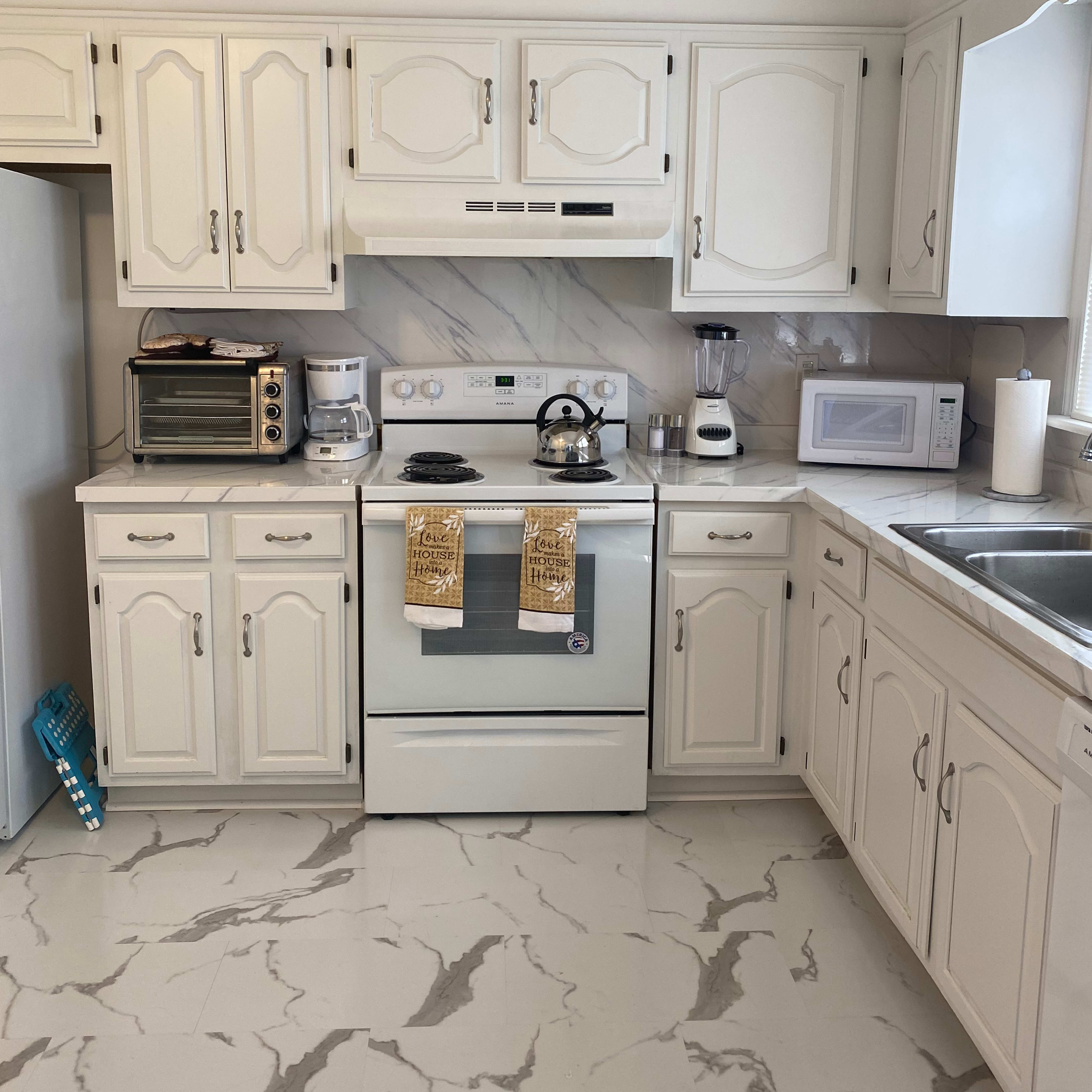 A white kitchen features a stove, microwave, and various appliances arranged around granite countertops and cabinets.