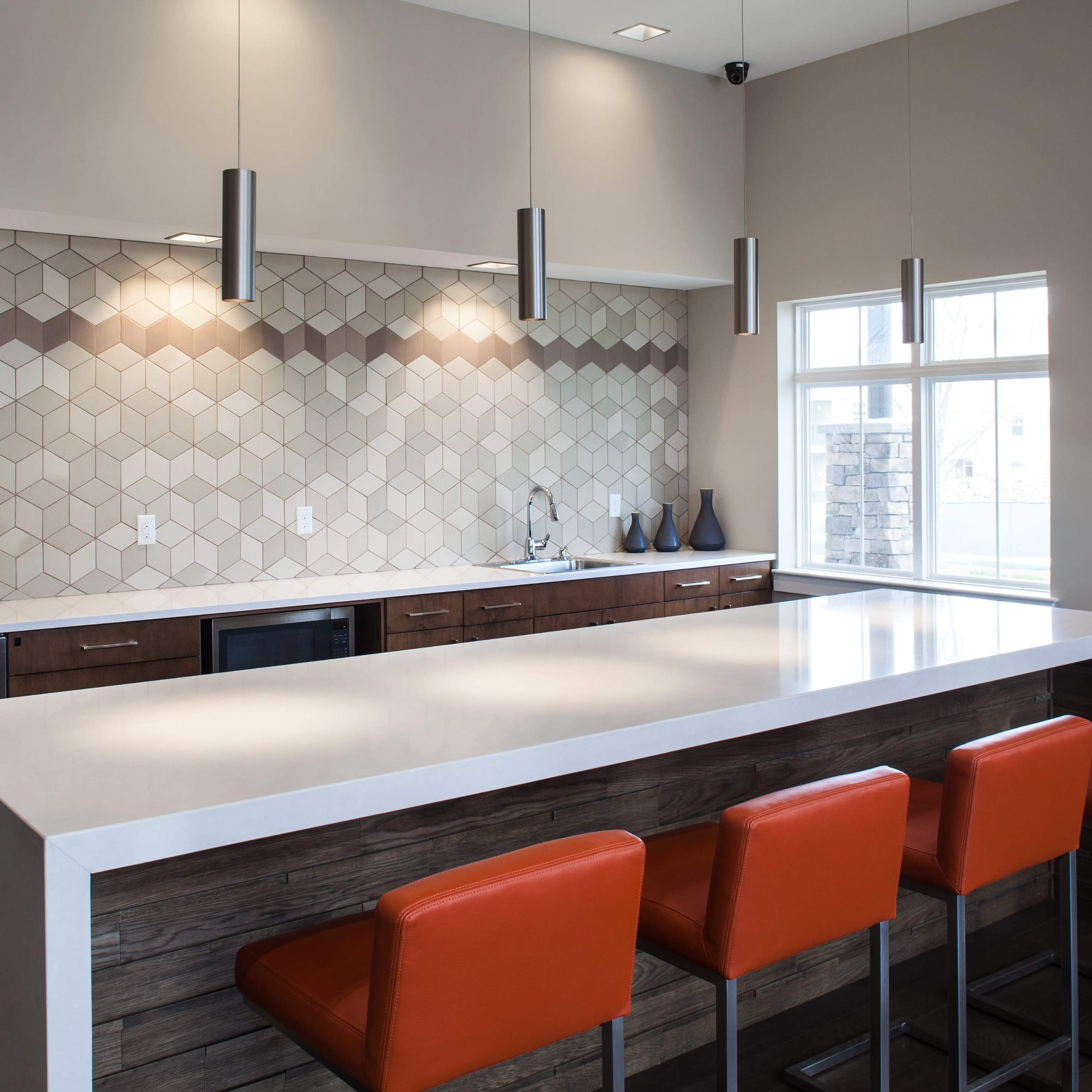 A modern kitchen features a hexagonal tiled backsplash, a long white countertop, and orange stools at the island.
