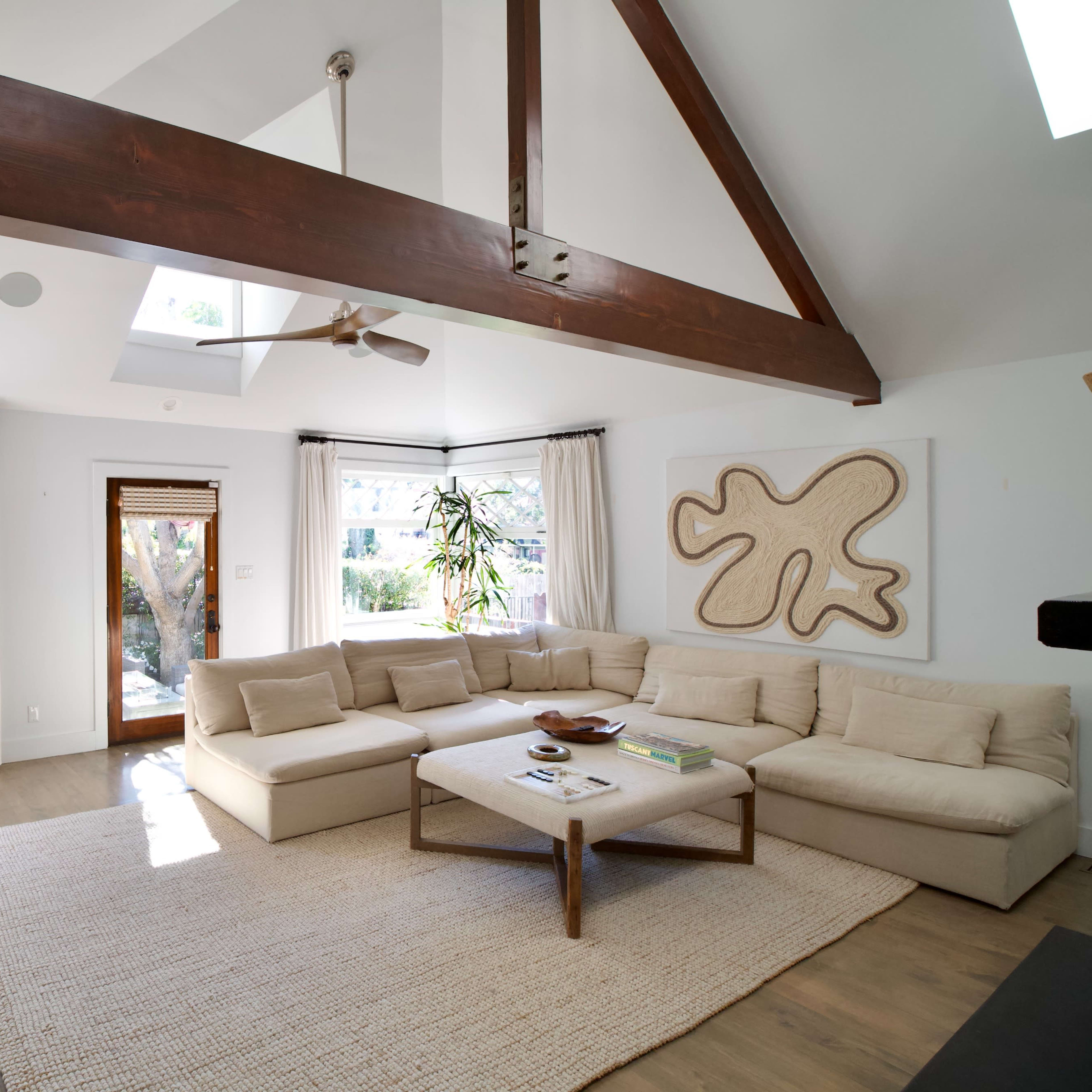 A spacious living room features a large sectional sofa, a coffee table, and natural light streaming in through windows and a skylight.