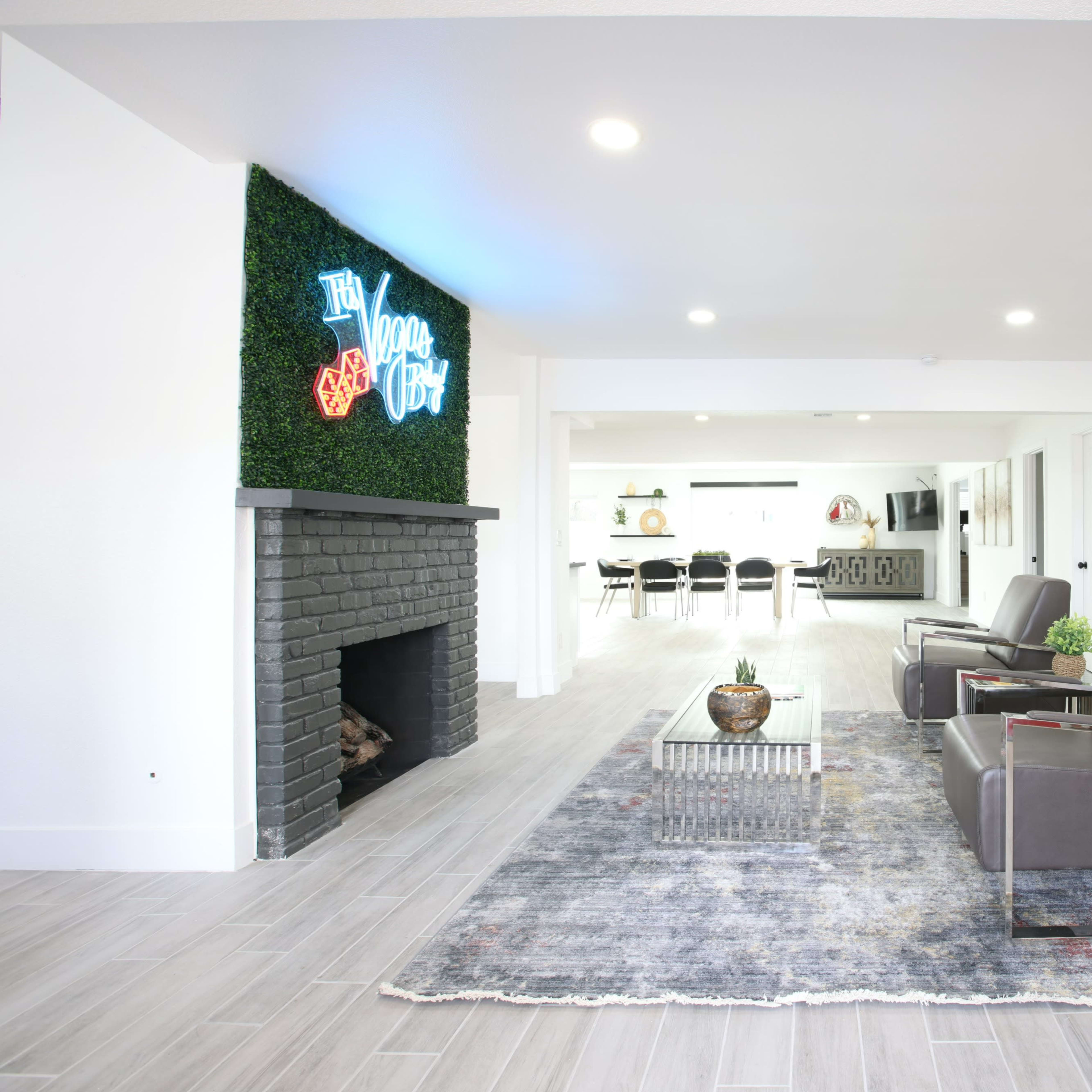 A modern, minimalist interior features gray armchairs, a decorative fireplace, and a wall with neon signage and artistic decor.