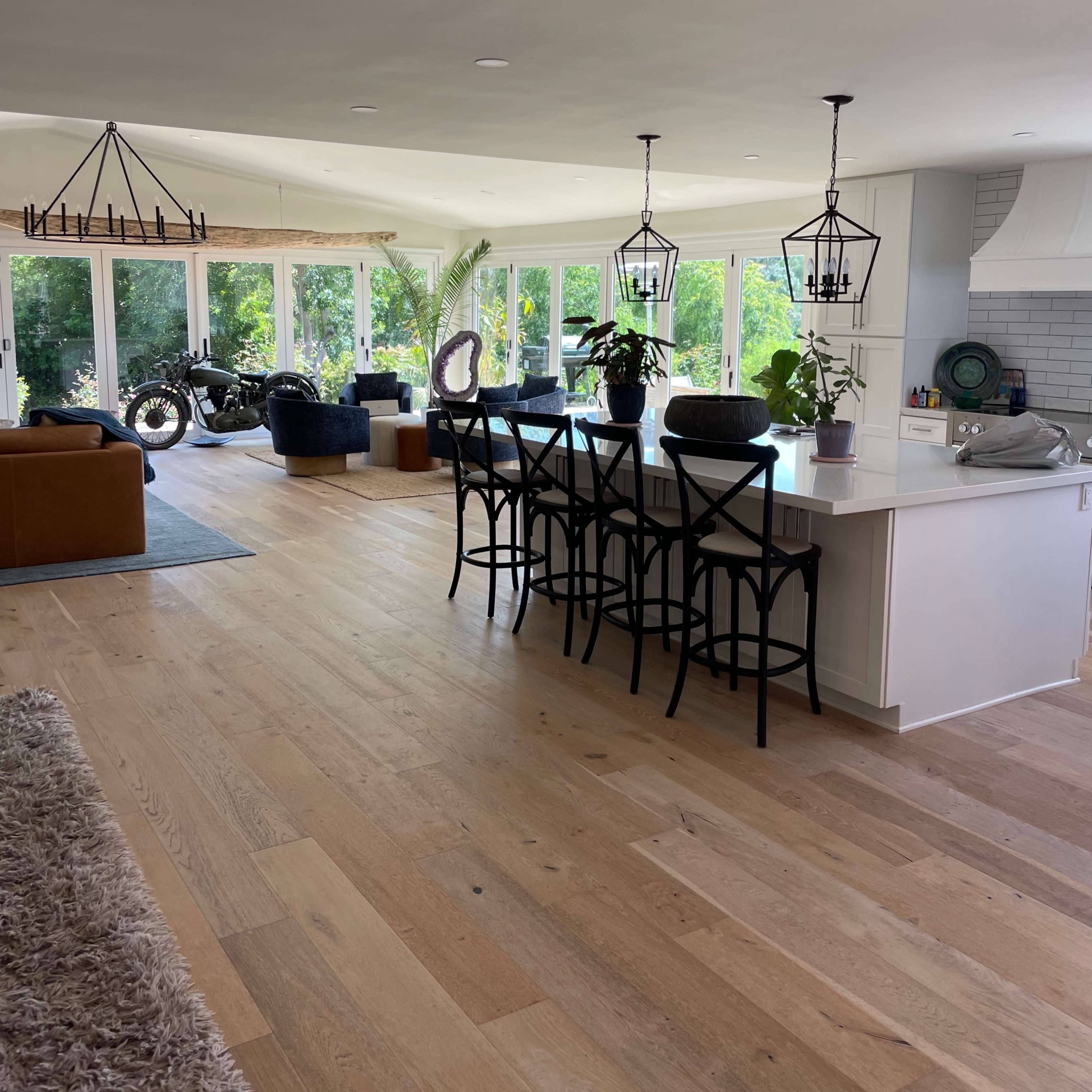 An open-concept living space featuring a kitchen with a long island and seating, a dining area, and large windows that provide natural light and views of greenery outside.