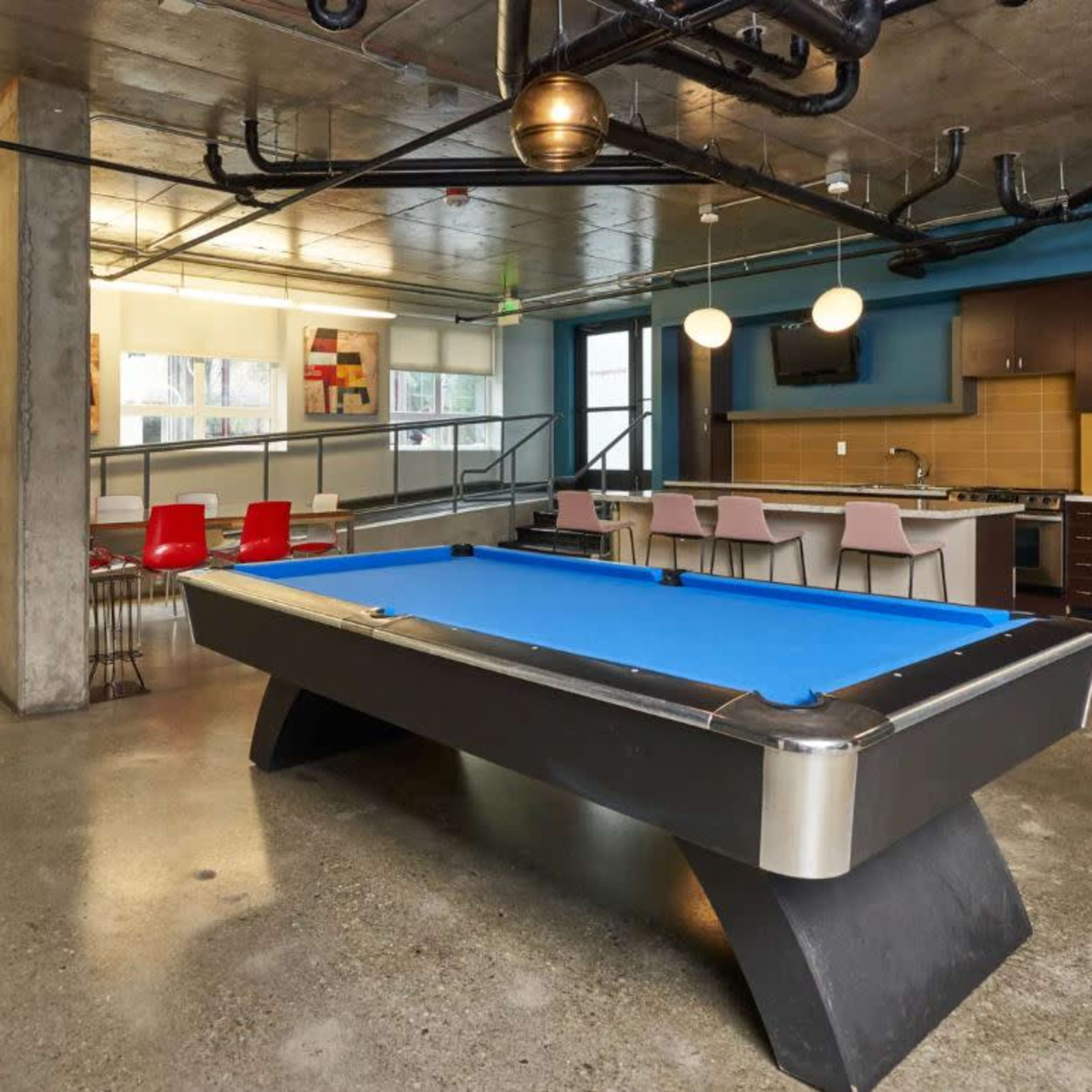 A modern game room with a blue pool table, a kitchenette, and seating areas.