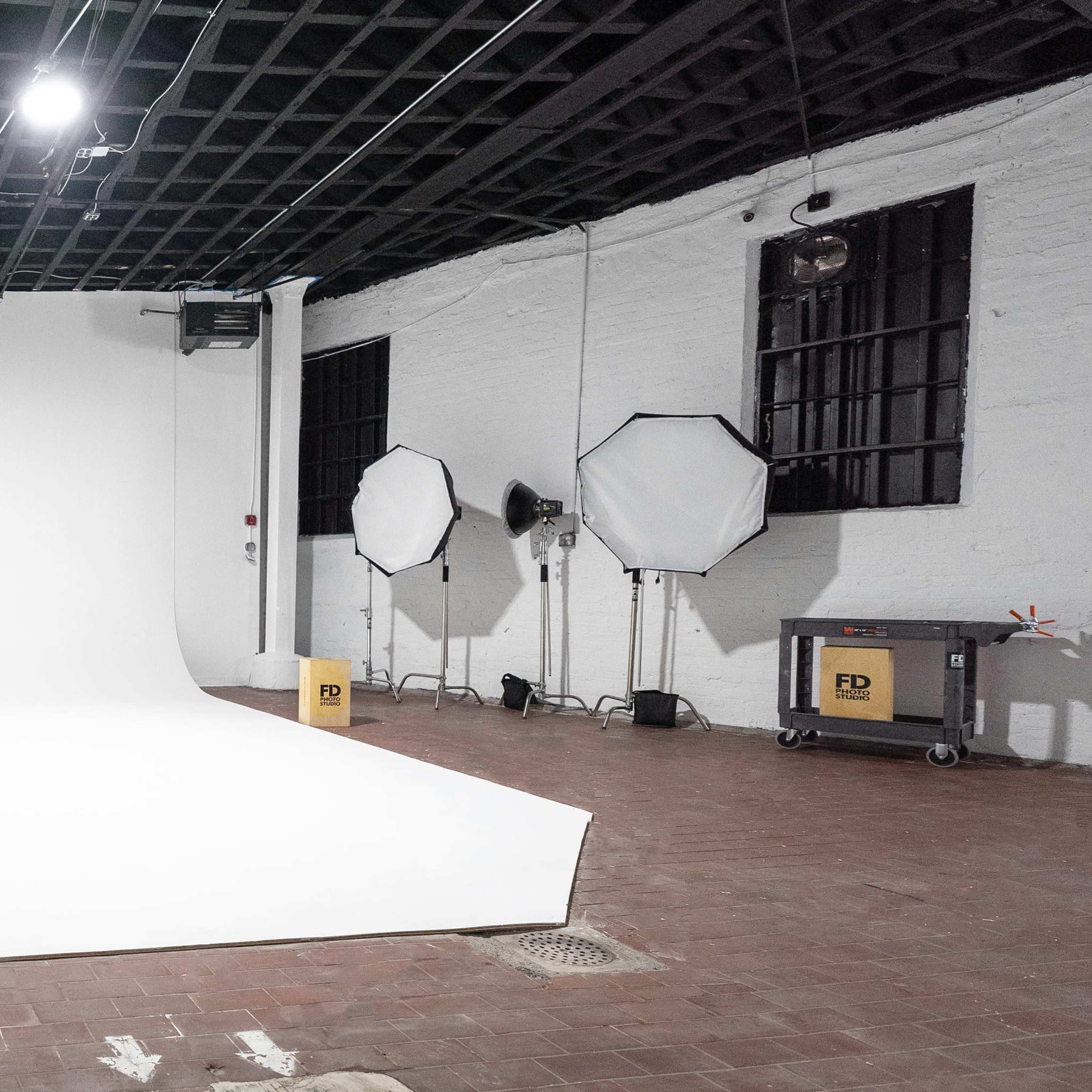 A photography studio with a seamless white backdrop, softbox lights, and a cart in a well-lit, empty space.