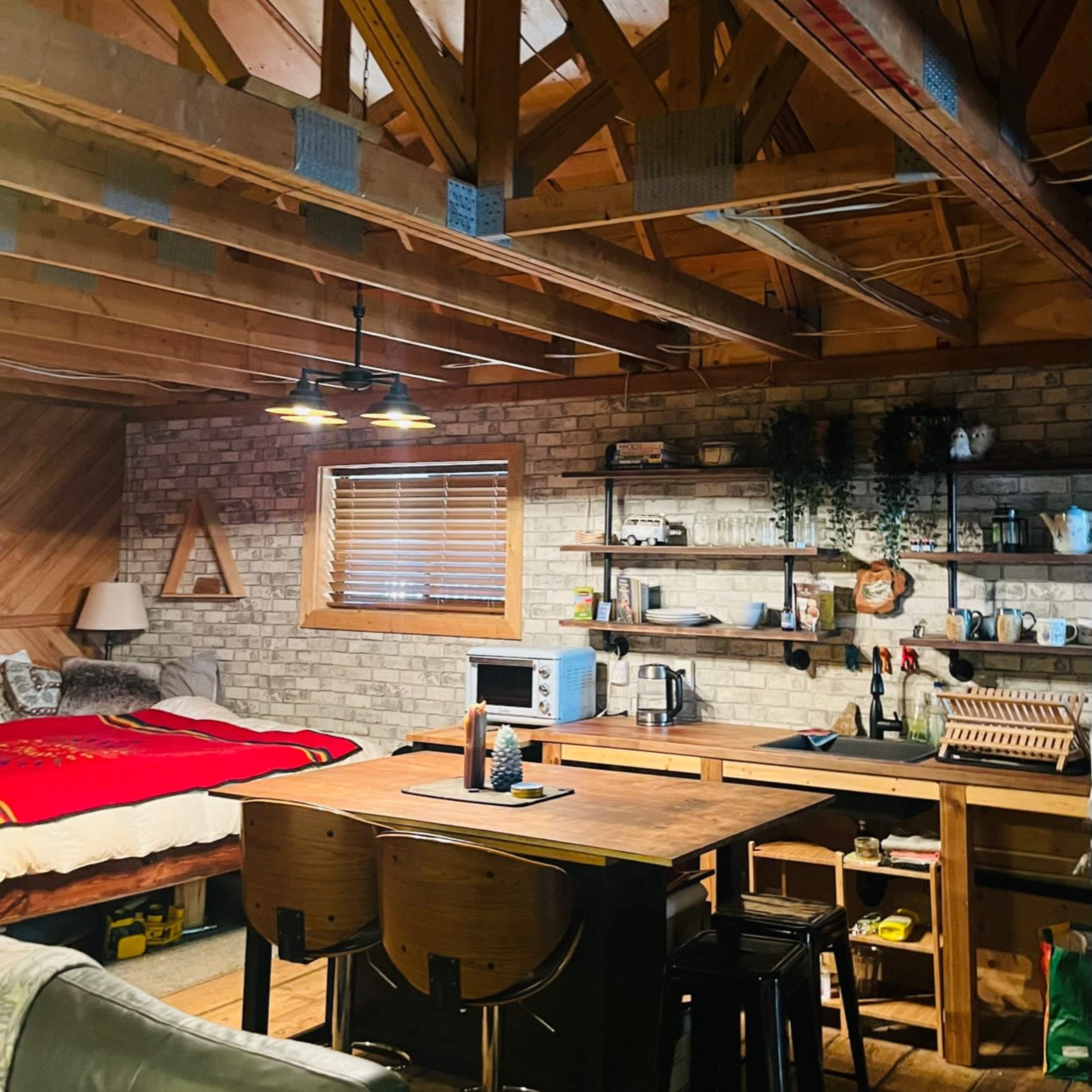 A cozy cabin interior features a bedroom area with a bed, a living space with a sofa, and a kitchen area complete with a table and various appliances.