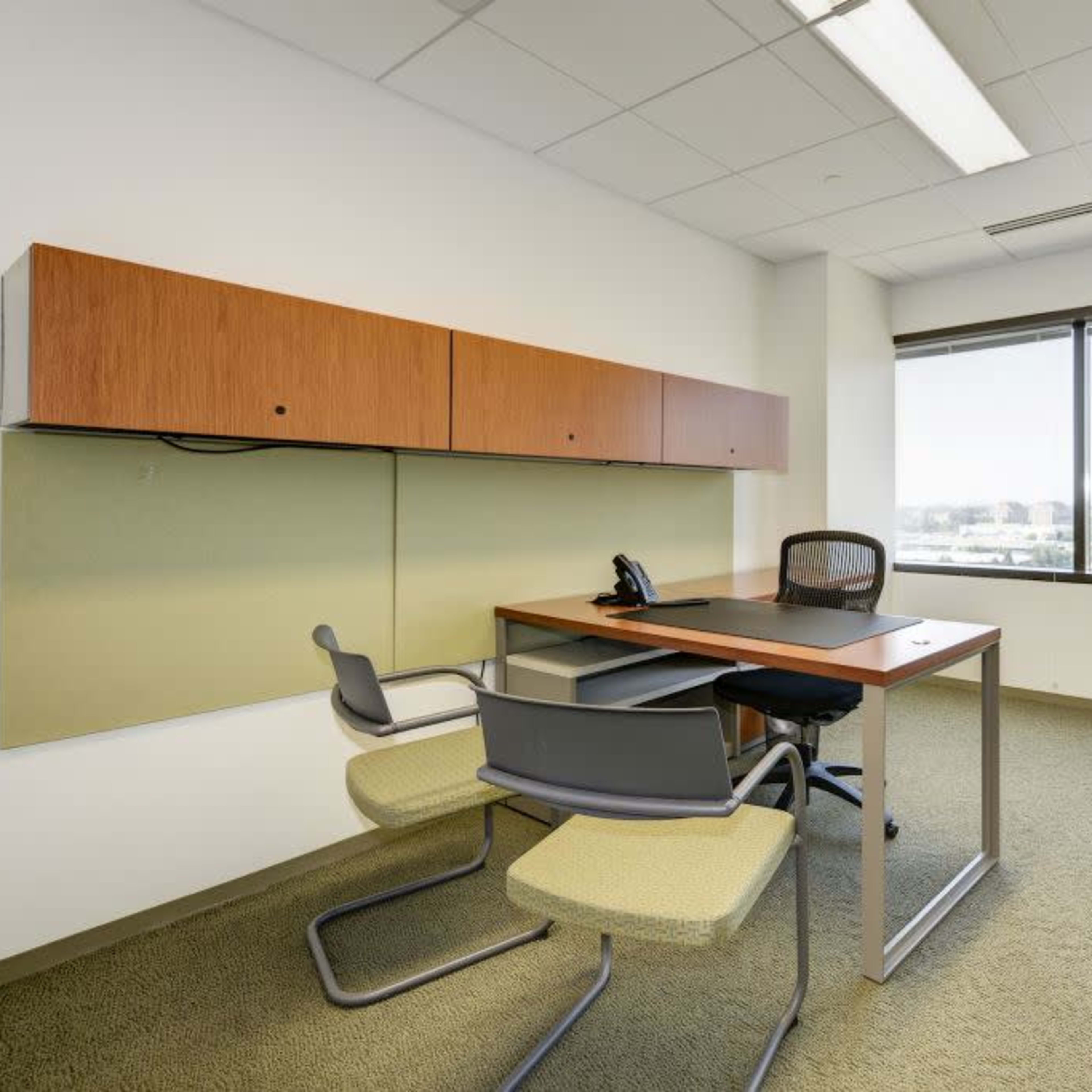 A minimalist office space featuring a desk with a chair, a telephone, and a wall-mounted storage unit beside a large window.