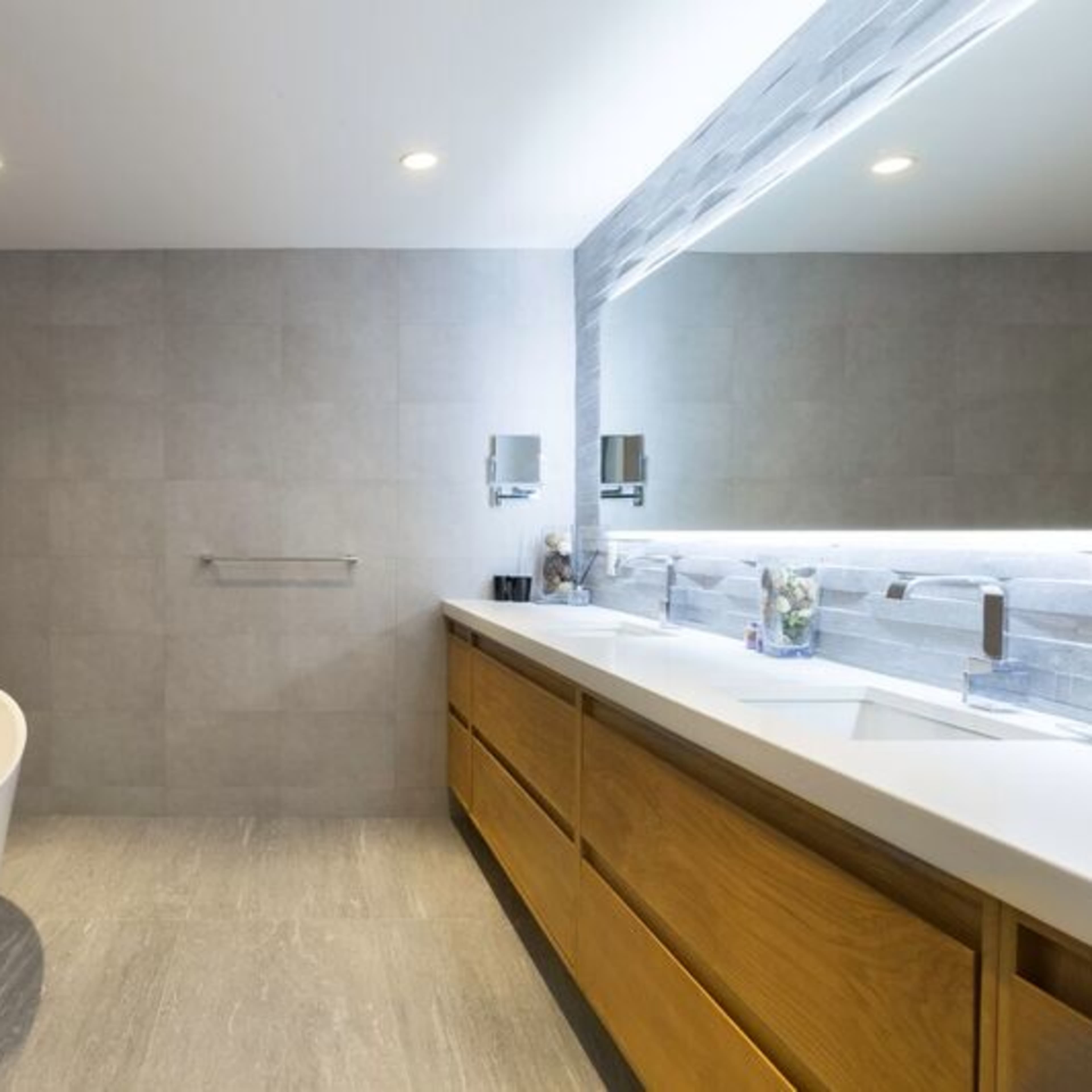 A modern bathroom featuring a freestanding white bathtub, dual sinks with a wooden vanity, and stone accent walls.
