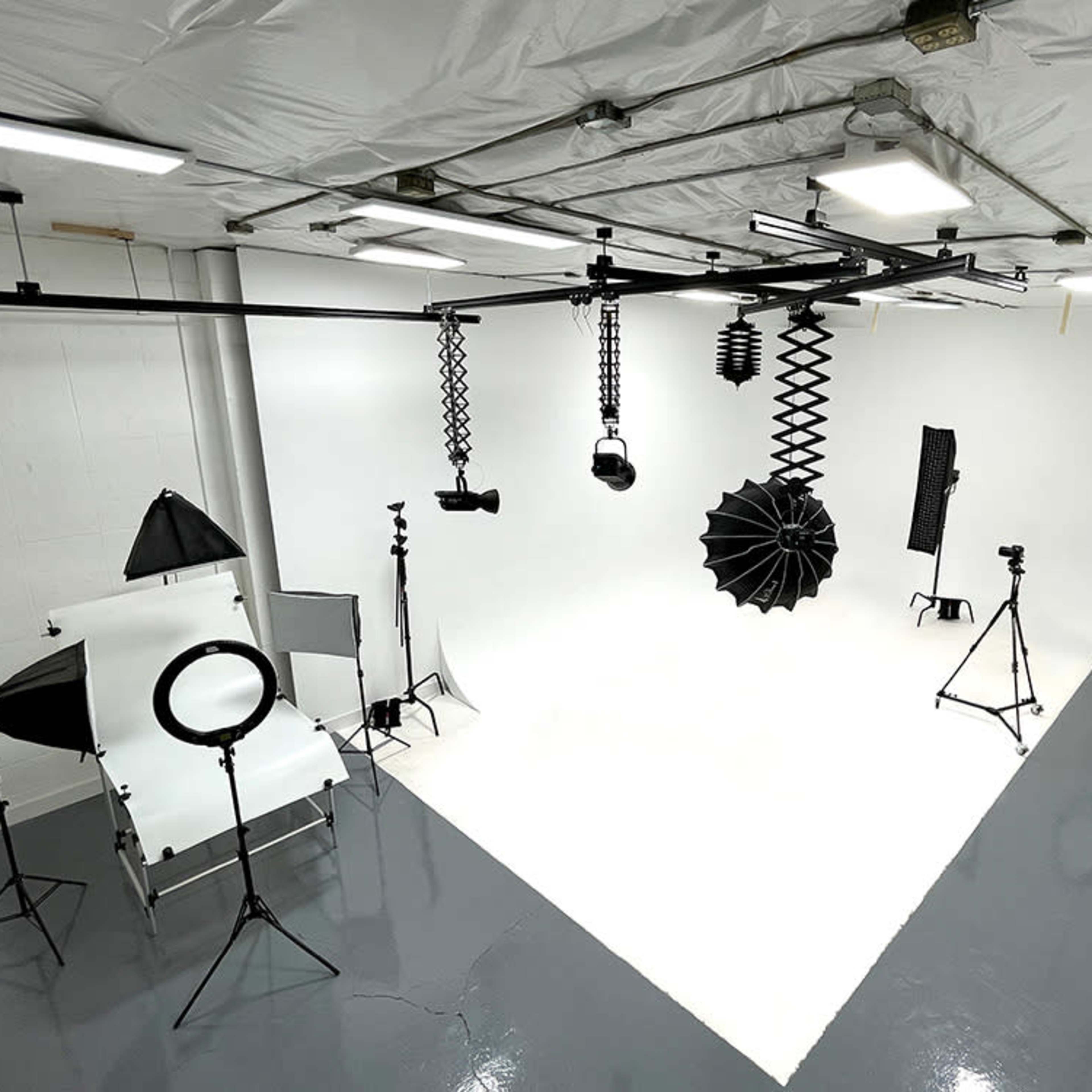 A photography studio with various lighting equipment, backdrops, and stands arranged in a white-walled space.