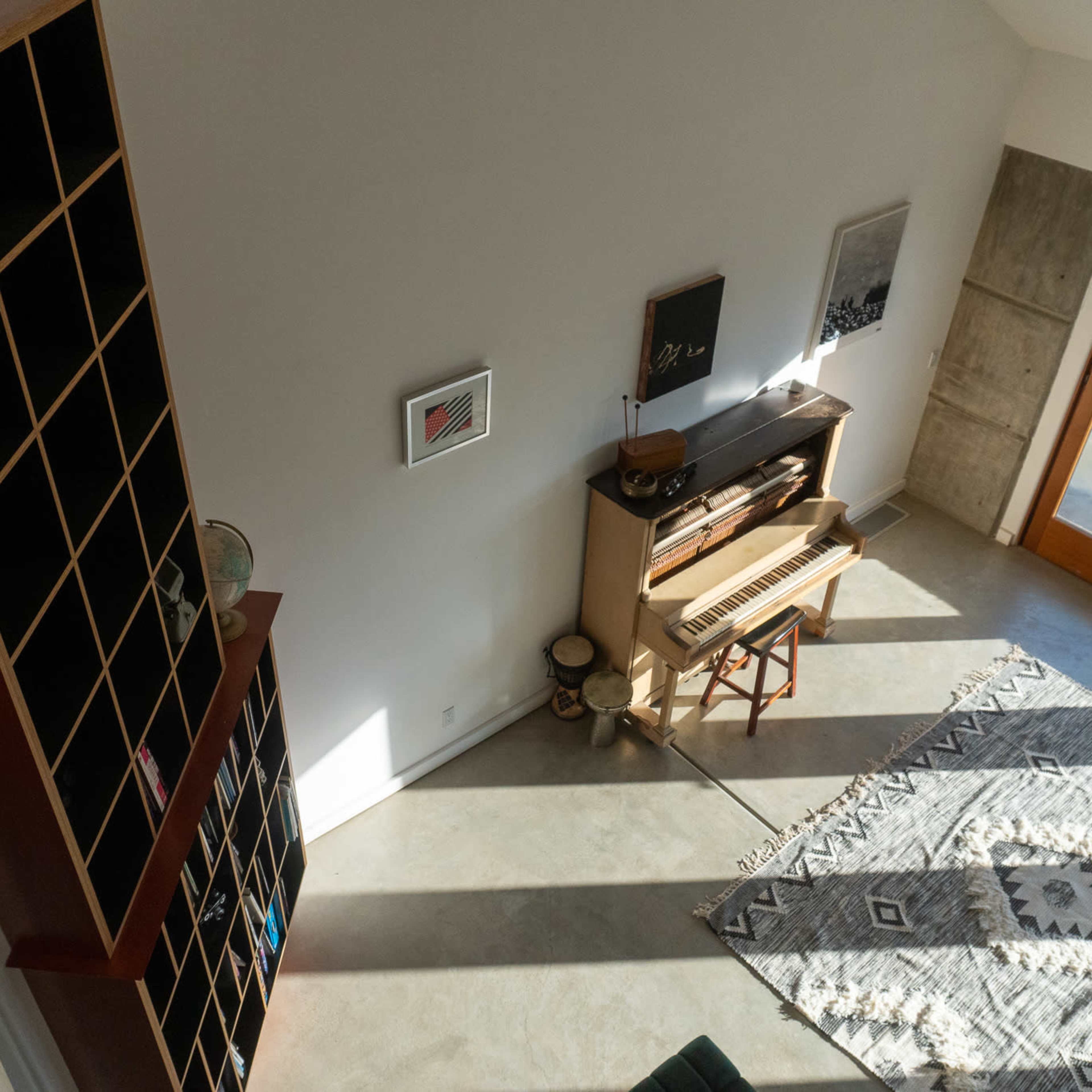 A modern interior space with a piano, a bookshelf, and large windows allowing natural light to fill the room.