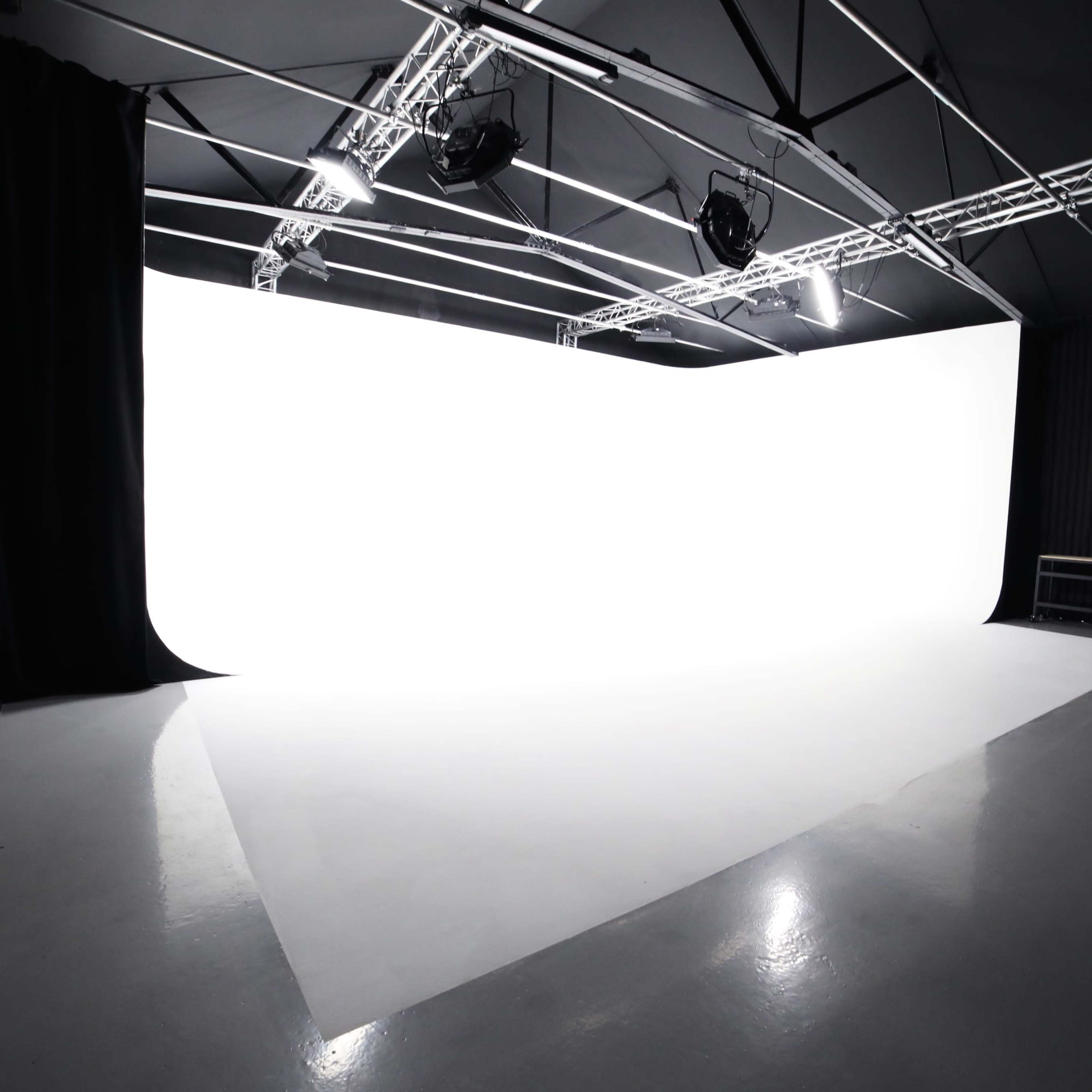 A photography studio with a large white backdrop and polished concrete floor under bright overhead lighting.