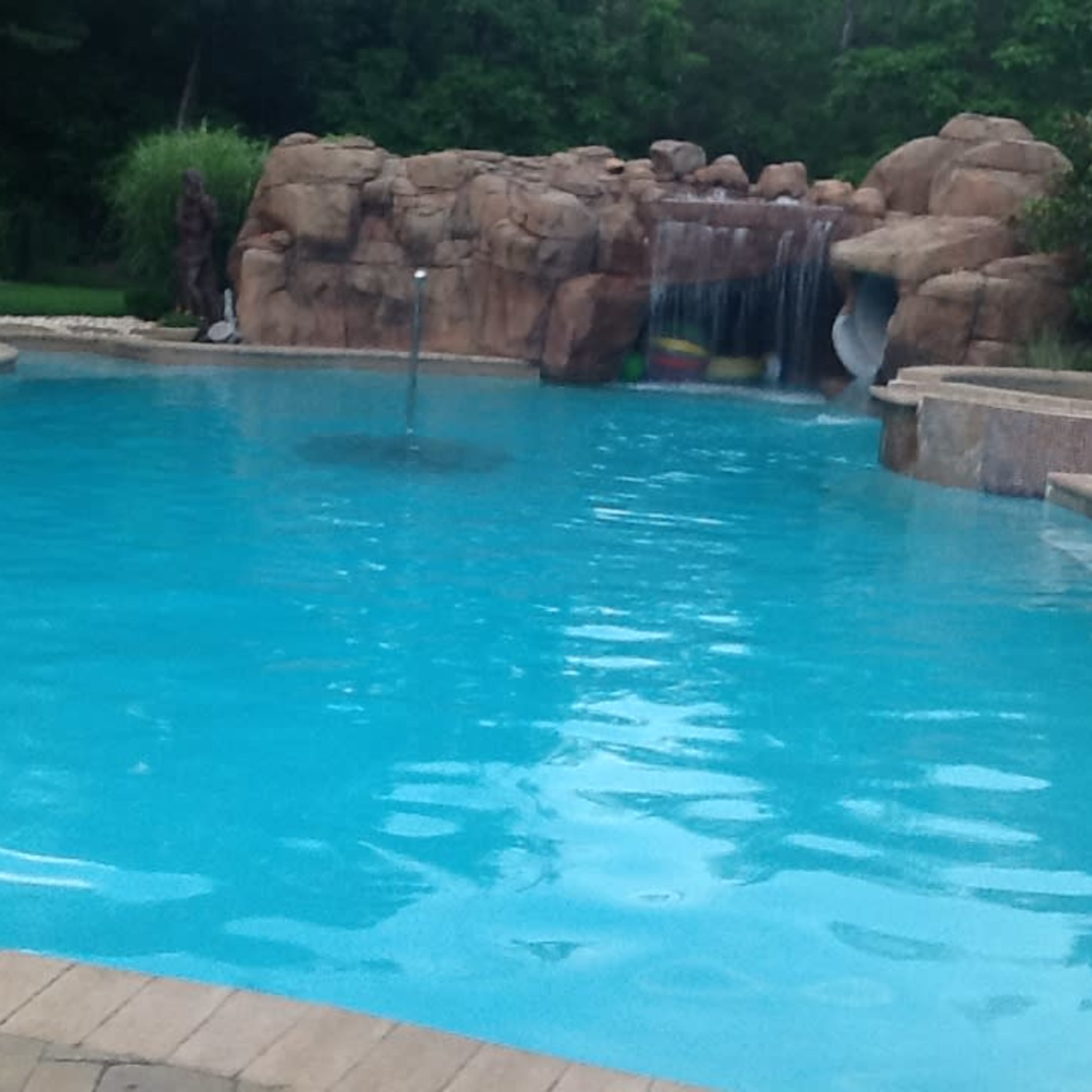A swimming pool with a rocky waterfall feature surrounded by greenery.