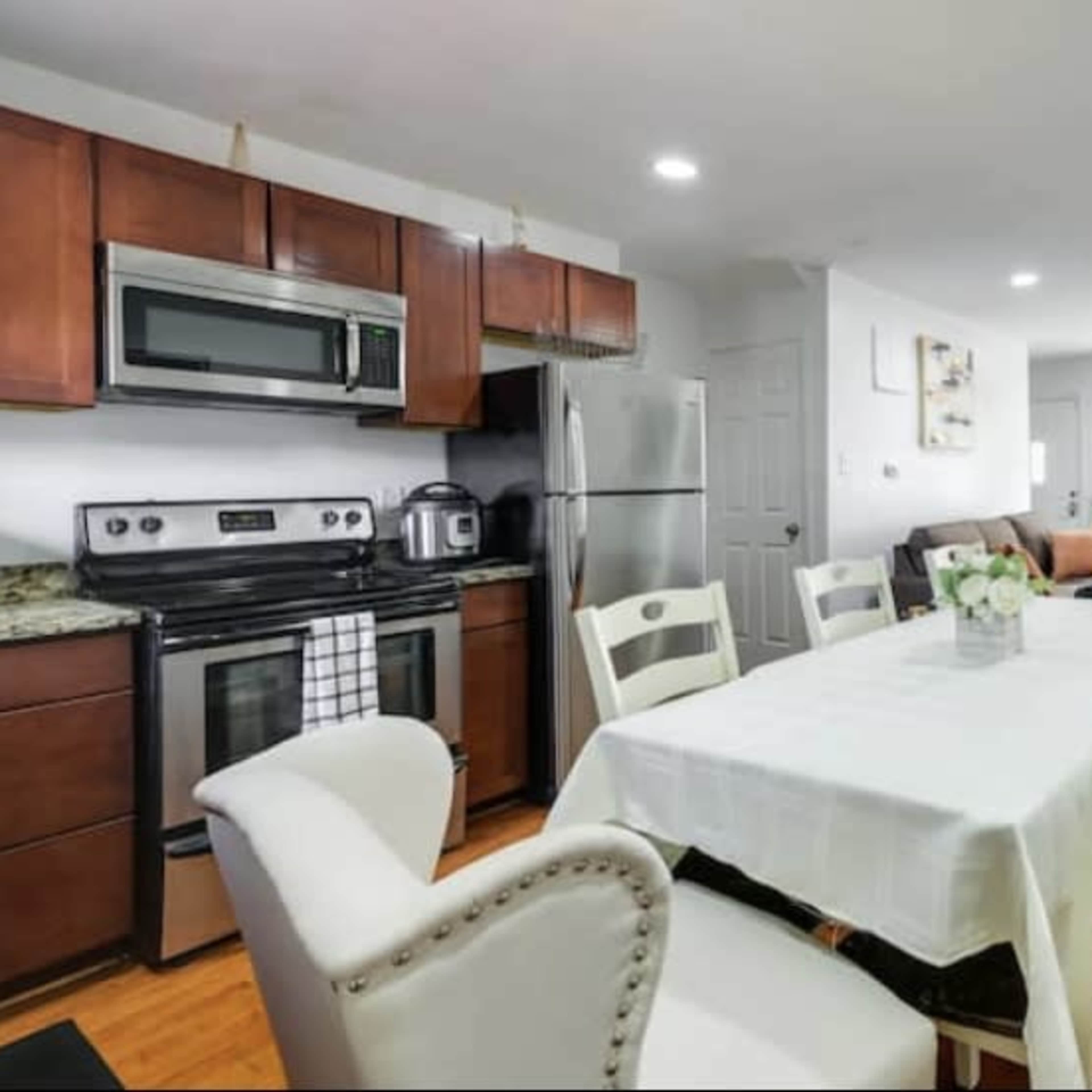 A modern kitchen and dining area featuring a table with white chairs, stainless steel appliances, and a cozy living room in the background.