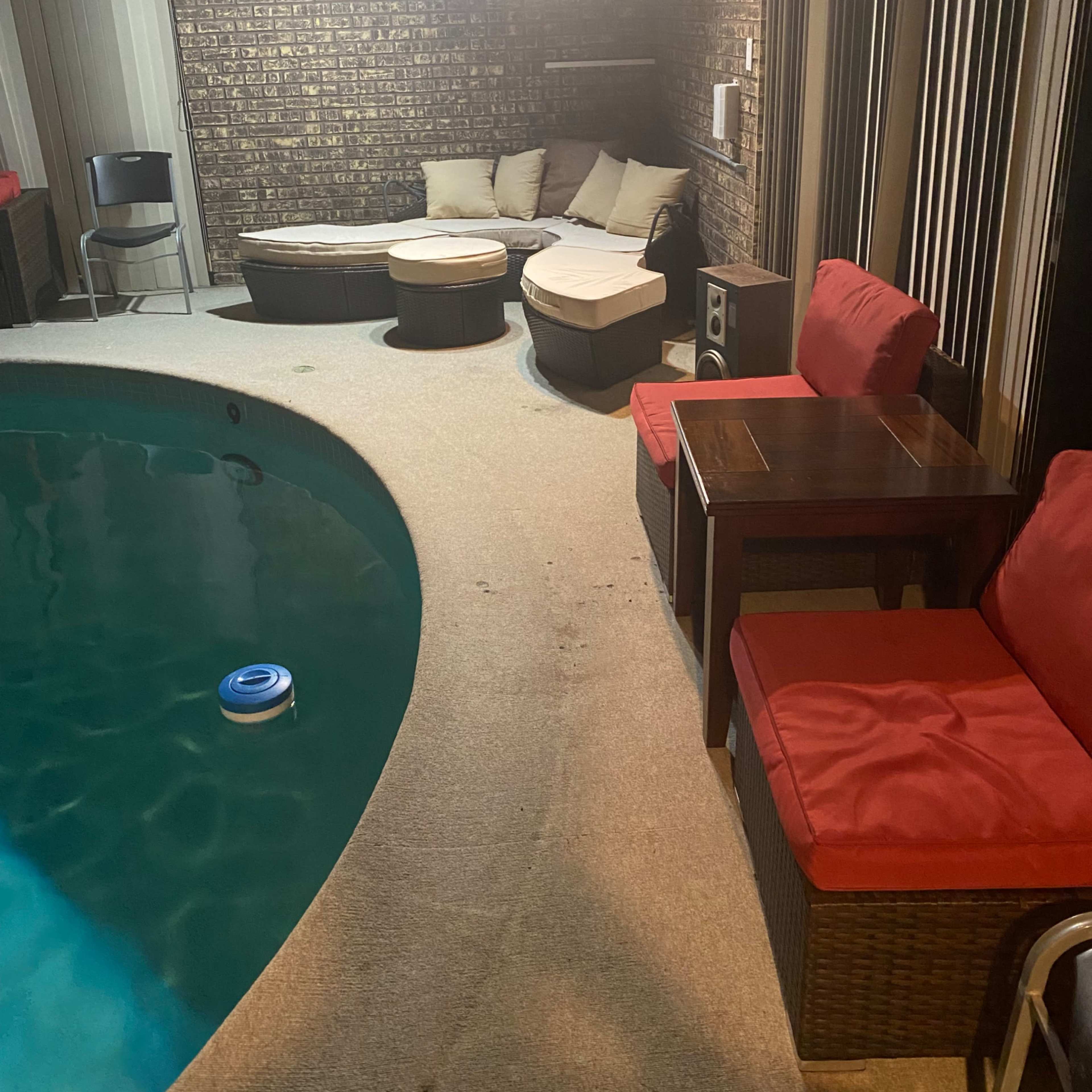 A private indoor pool area with a circular pool, wicker seating, and a wooden table beside it.