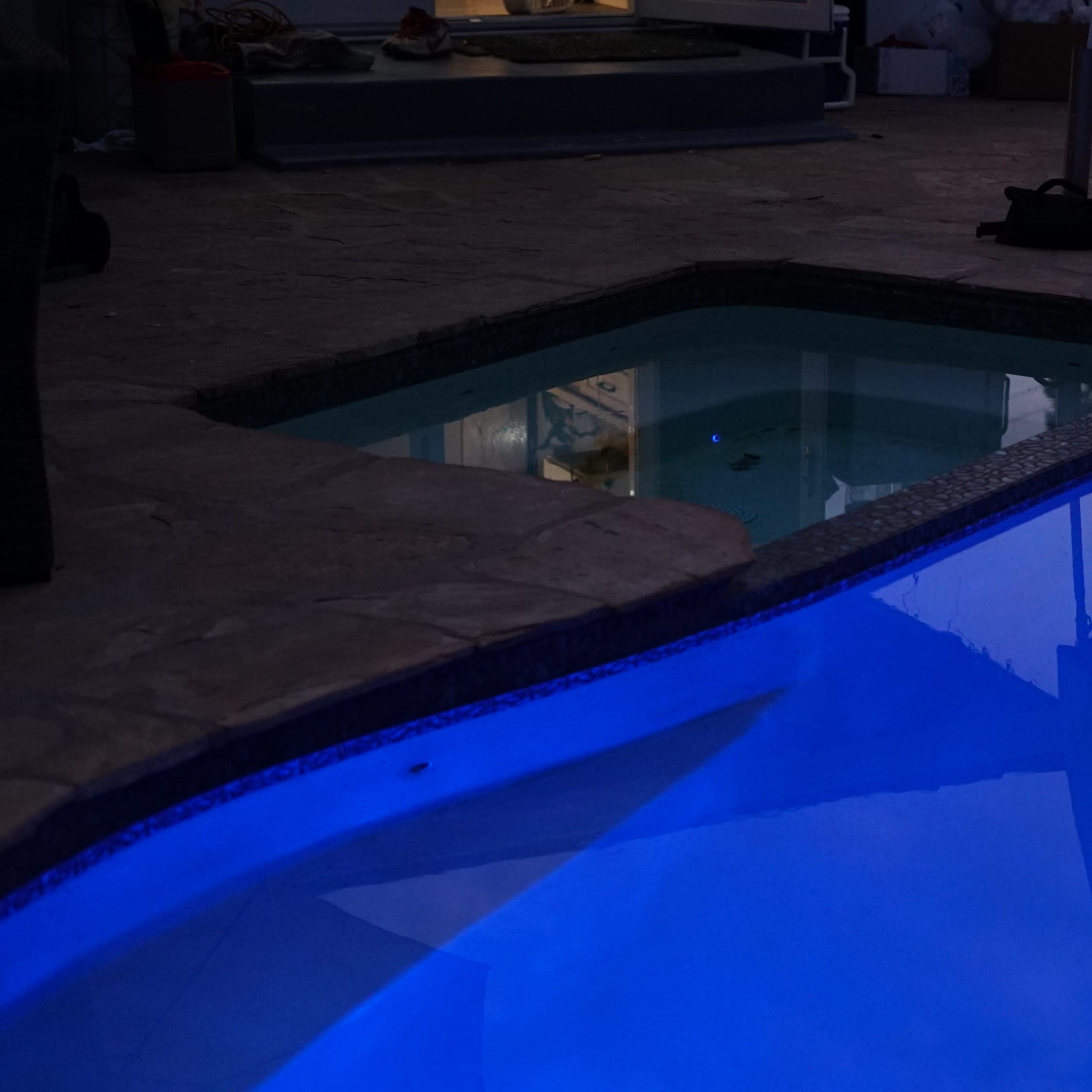 A swimming pool area at night, featuring blue lighting and reflections on the water's surface.