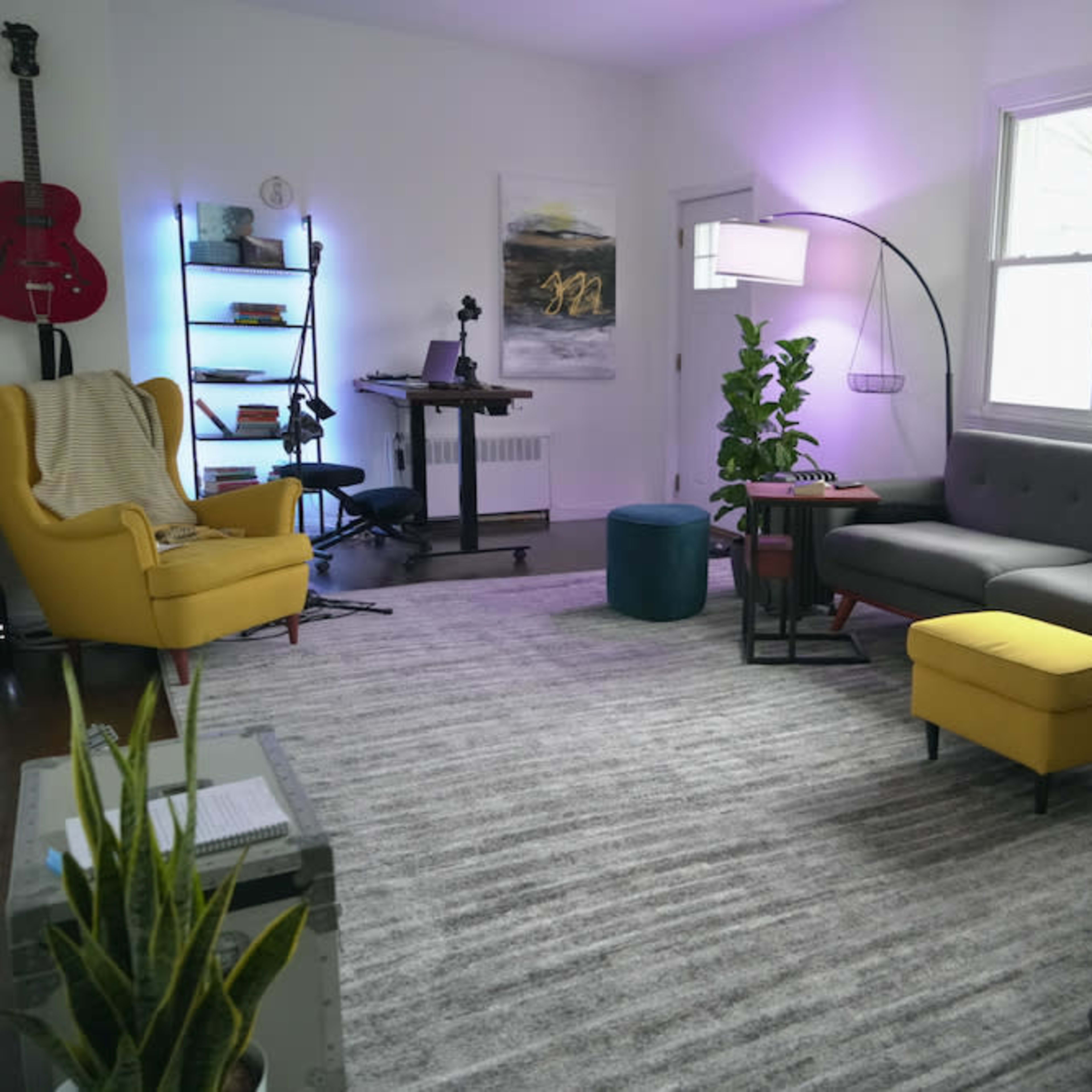 A modern living room with a gray sectional sofa, yellow accent chair, green plants, and a desk setup in the corner.