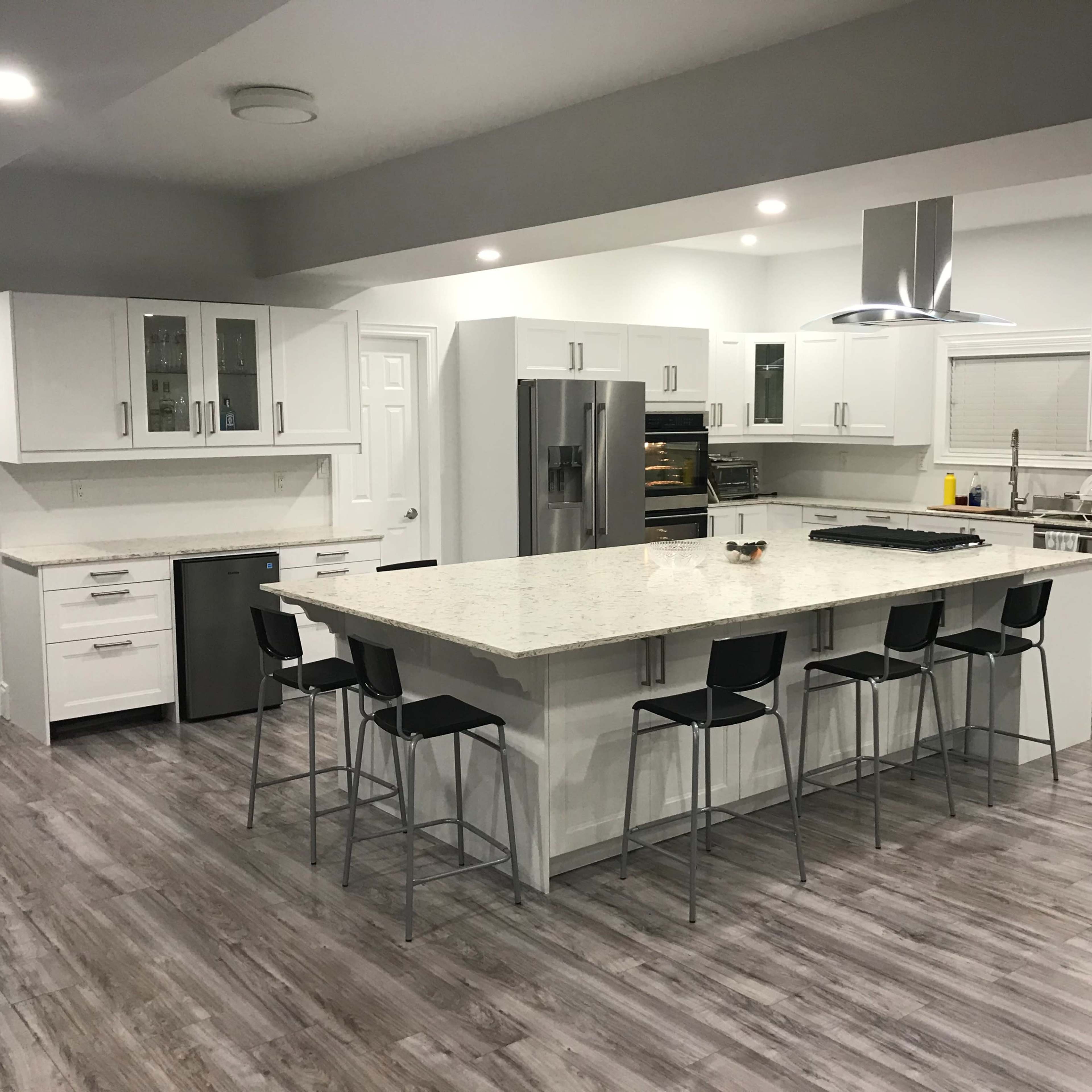 A modern kitchen featuring a large island with bar stools, white cabinetry, and stainless steel appliances.