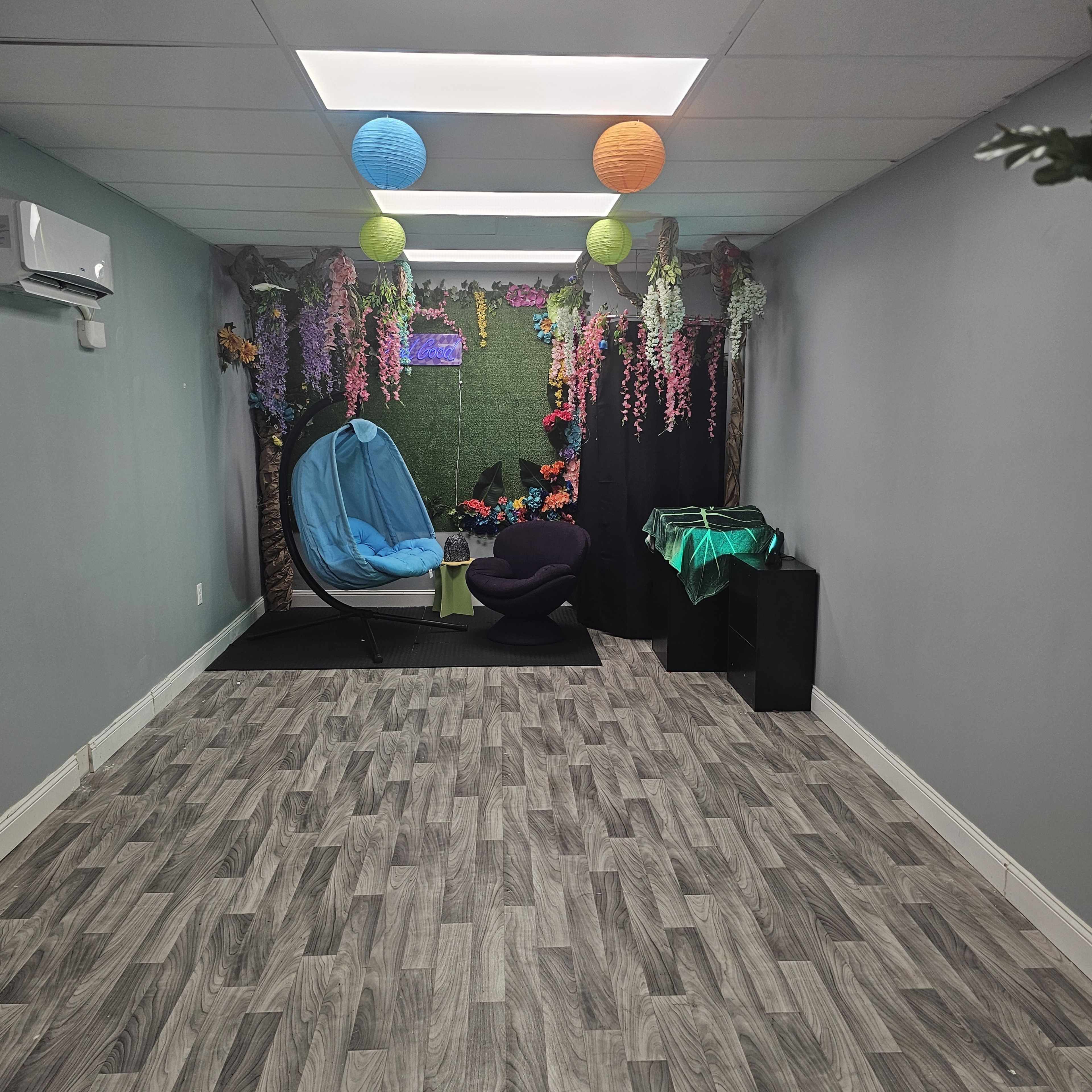 A room decorated with colorful lanterns and artificial flowers, featuring a blue hammock and a green mat on a wooden floor.